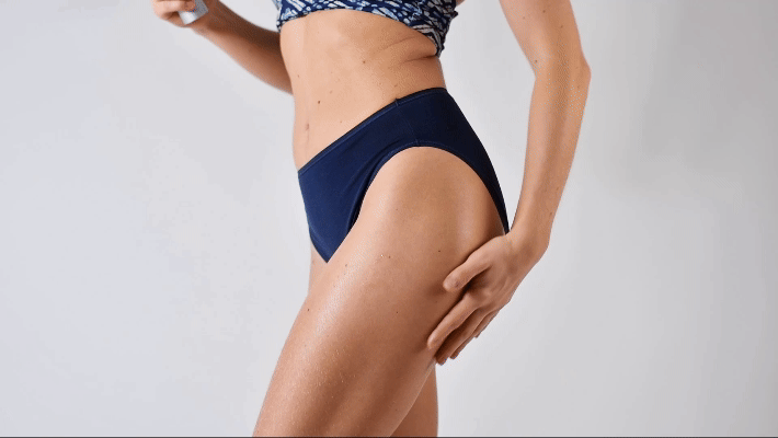 Close-up of a woman's midsection and upper thigh wearing dark blue underwear, with water droplets on her skin.
