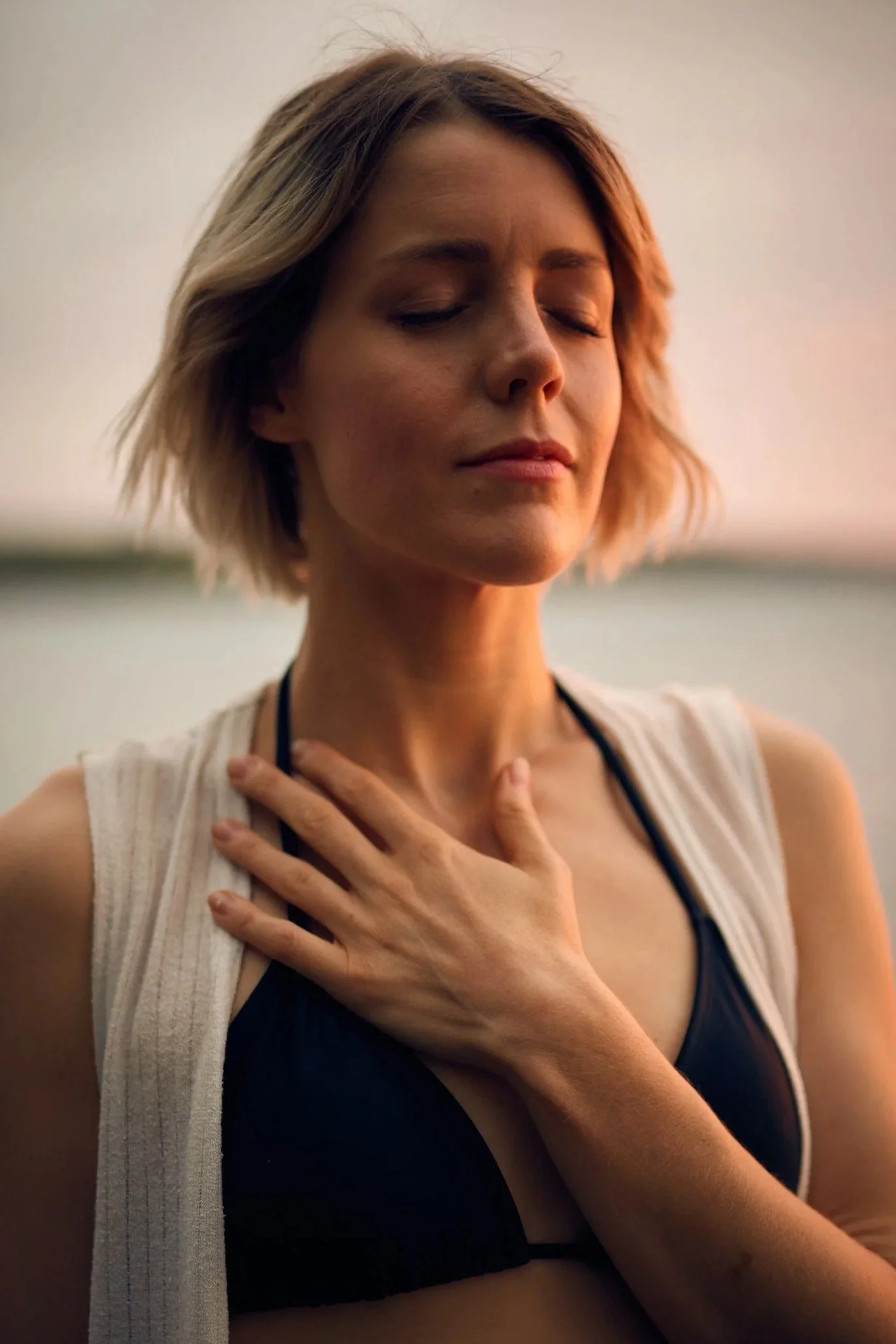 A woman with closed eyes holds a hand to her chest, appearing calm and peaceful in soft natural light.