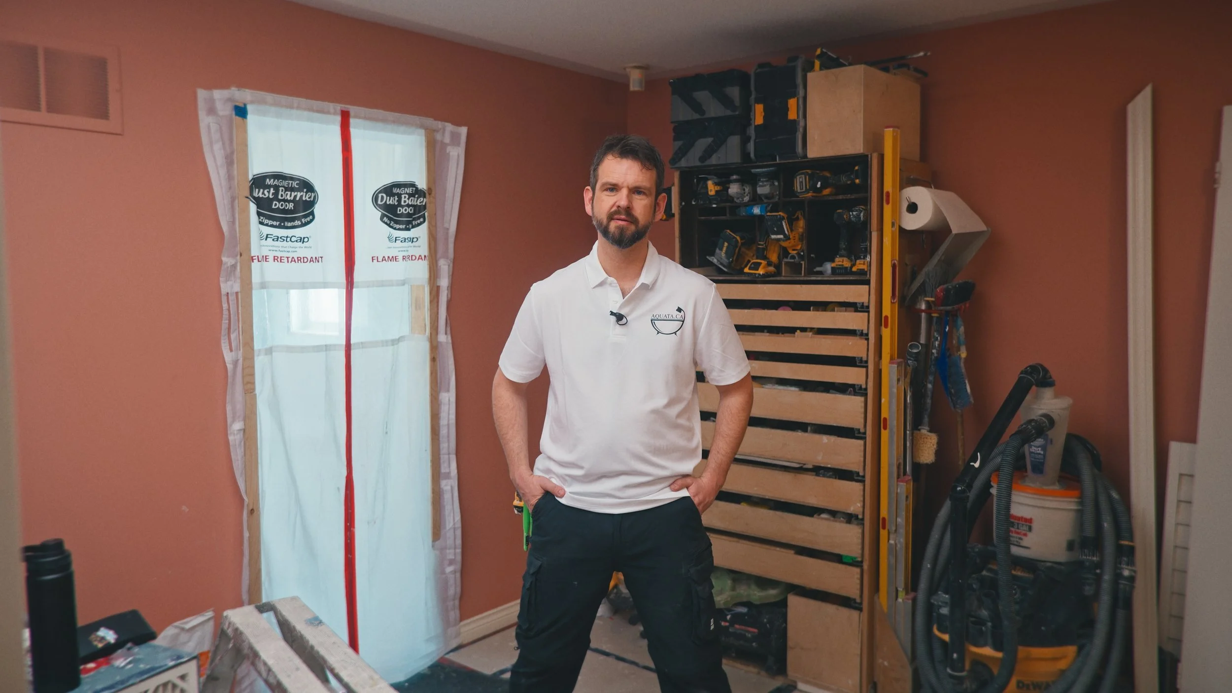 A man with a beard and dark hair standing in a partially renovated room. The room has construction tools, it's an example image of the testimonial video shooting service