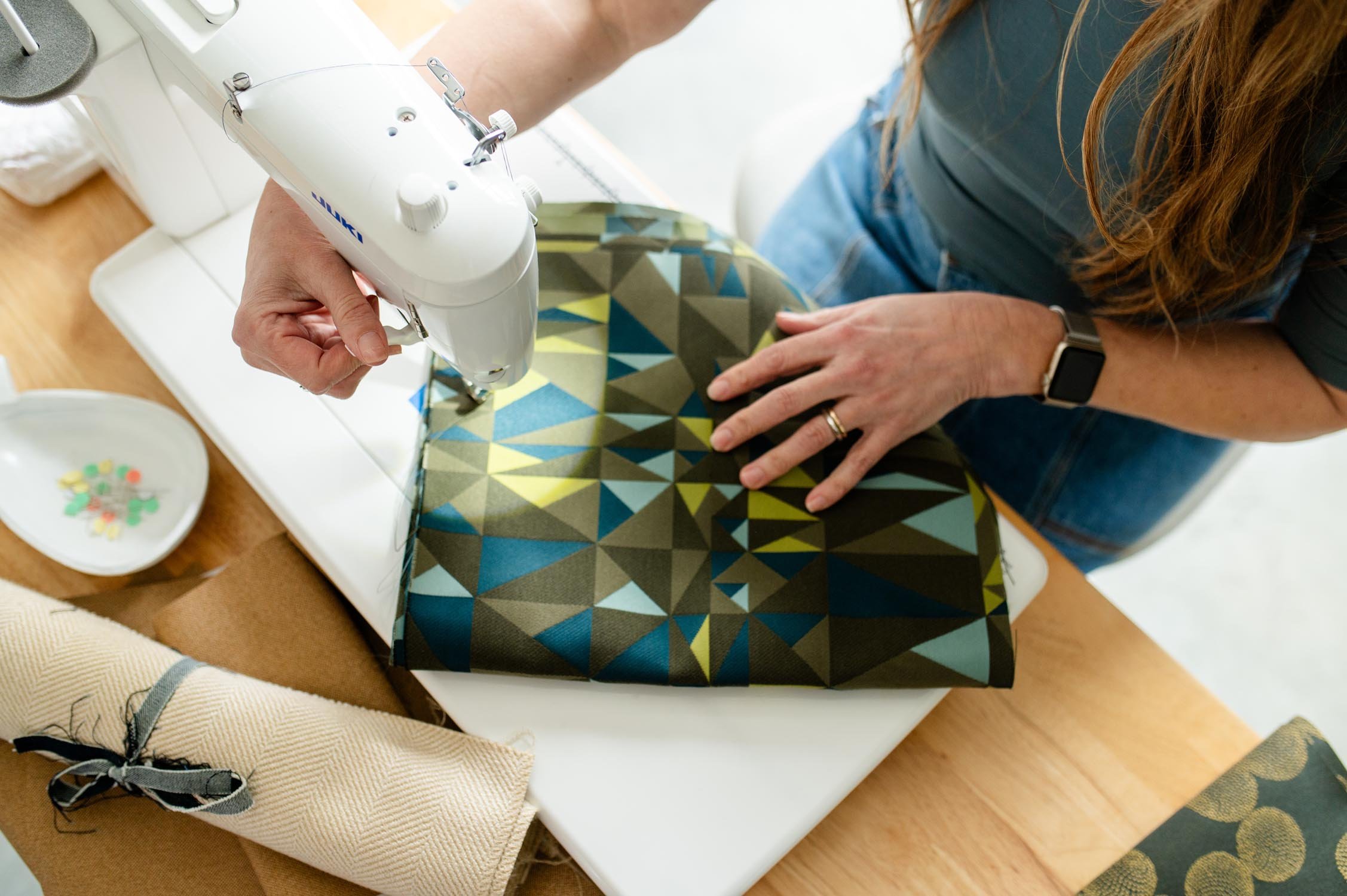 Tiffany sewing colorful geometric patterned fabric using a sewing machine on a table in Test Patch Studio.