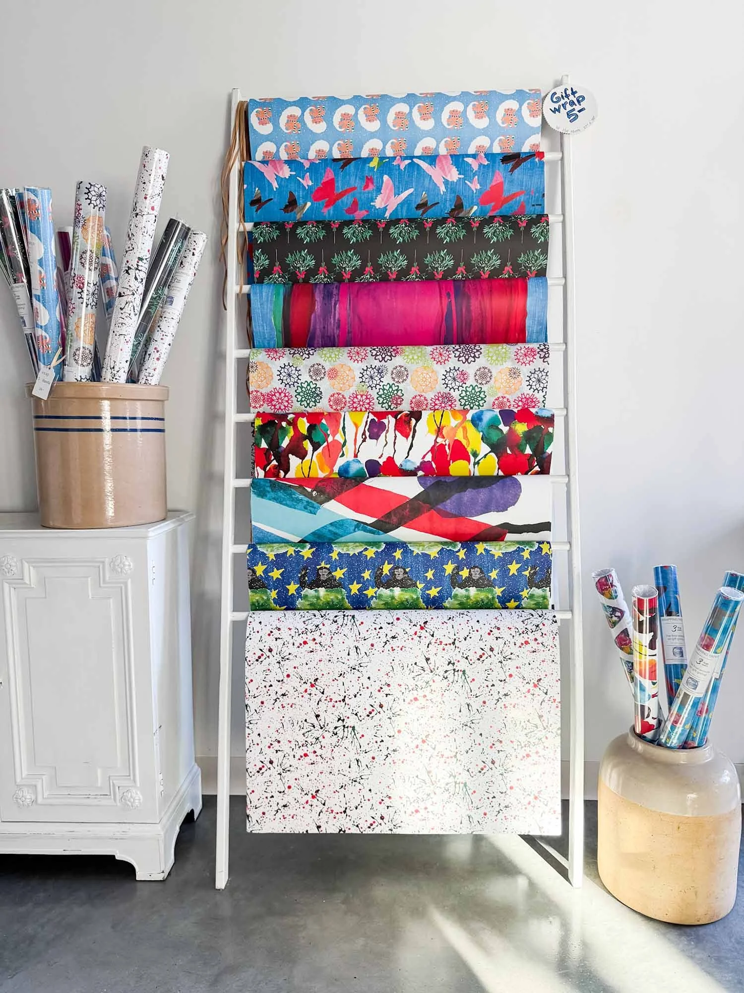 Display of various gift wraps with holiday and abstract designs on a white rack, with rolls of wrapping paper on both sides.