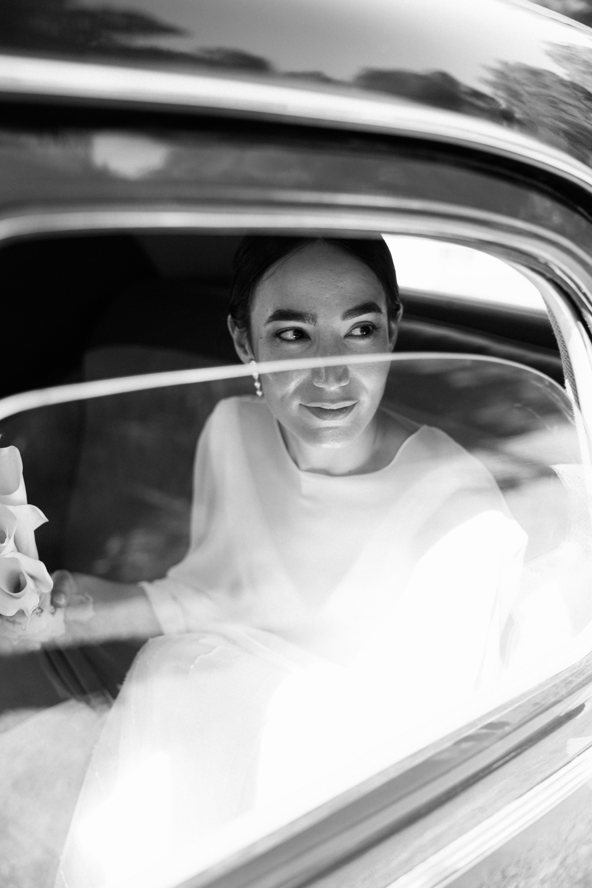 Mujer con vestido de novia, mirando por la ventana de un coche clásico.