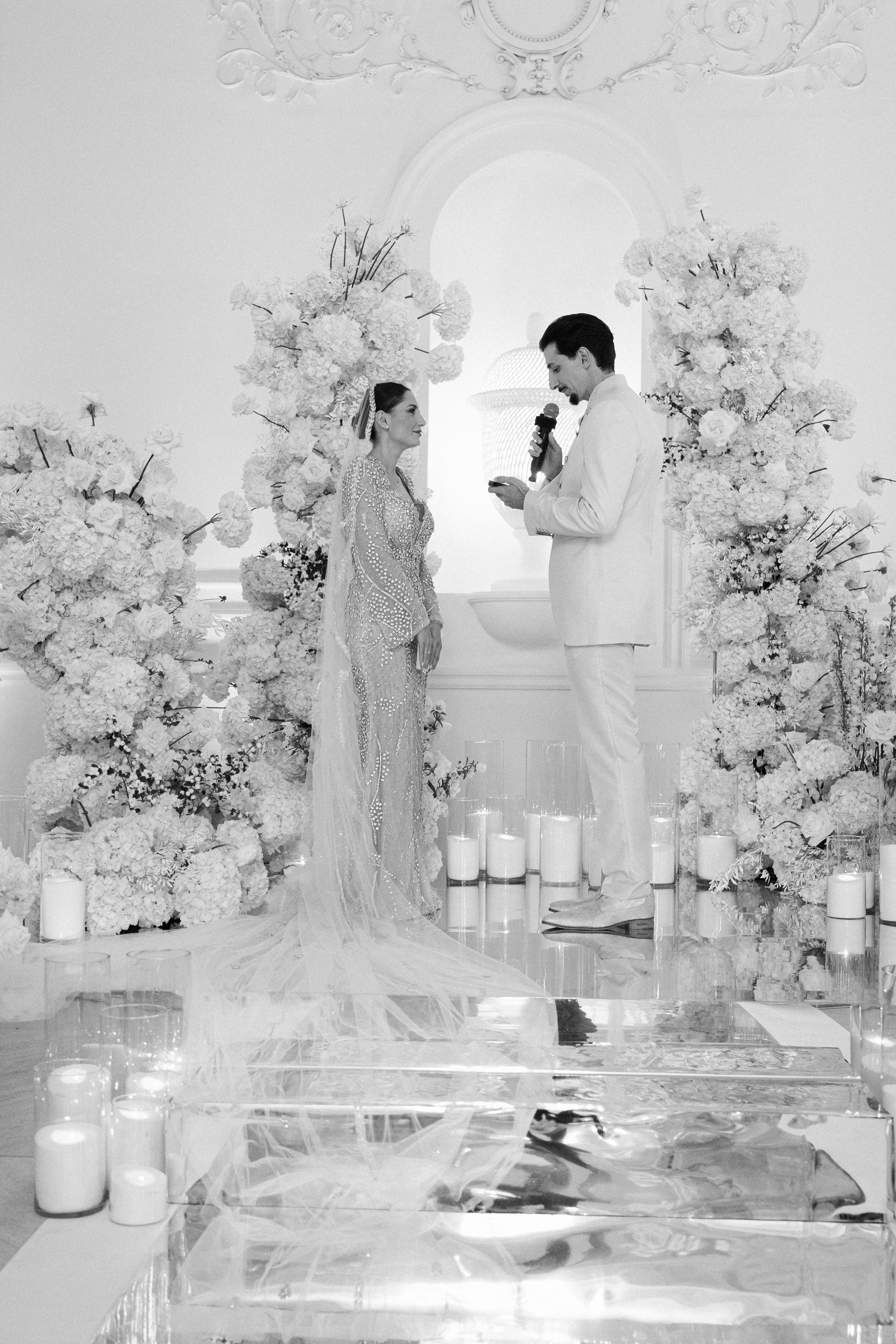 Pareja casándose en una ceremonia nupcial con decoraciones de flores blancas, velas y fondo elegante.