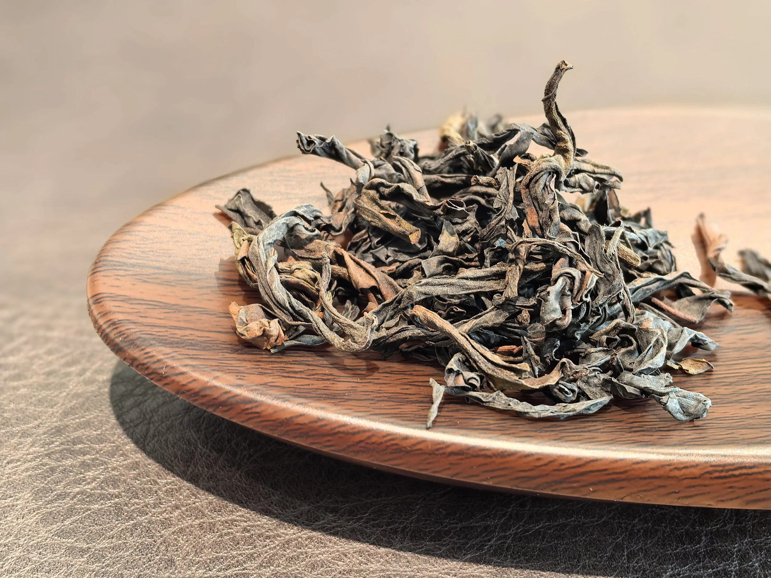 Dried loose tea leaves on a round wooden plate.