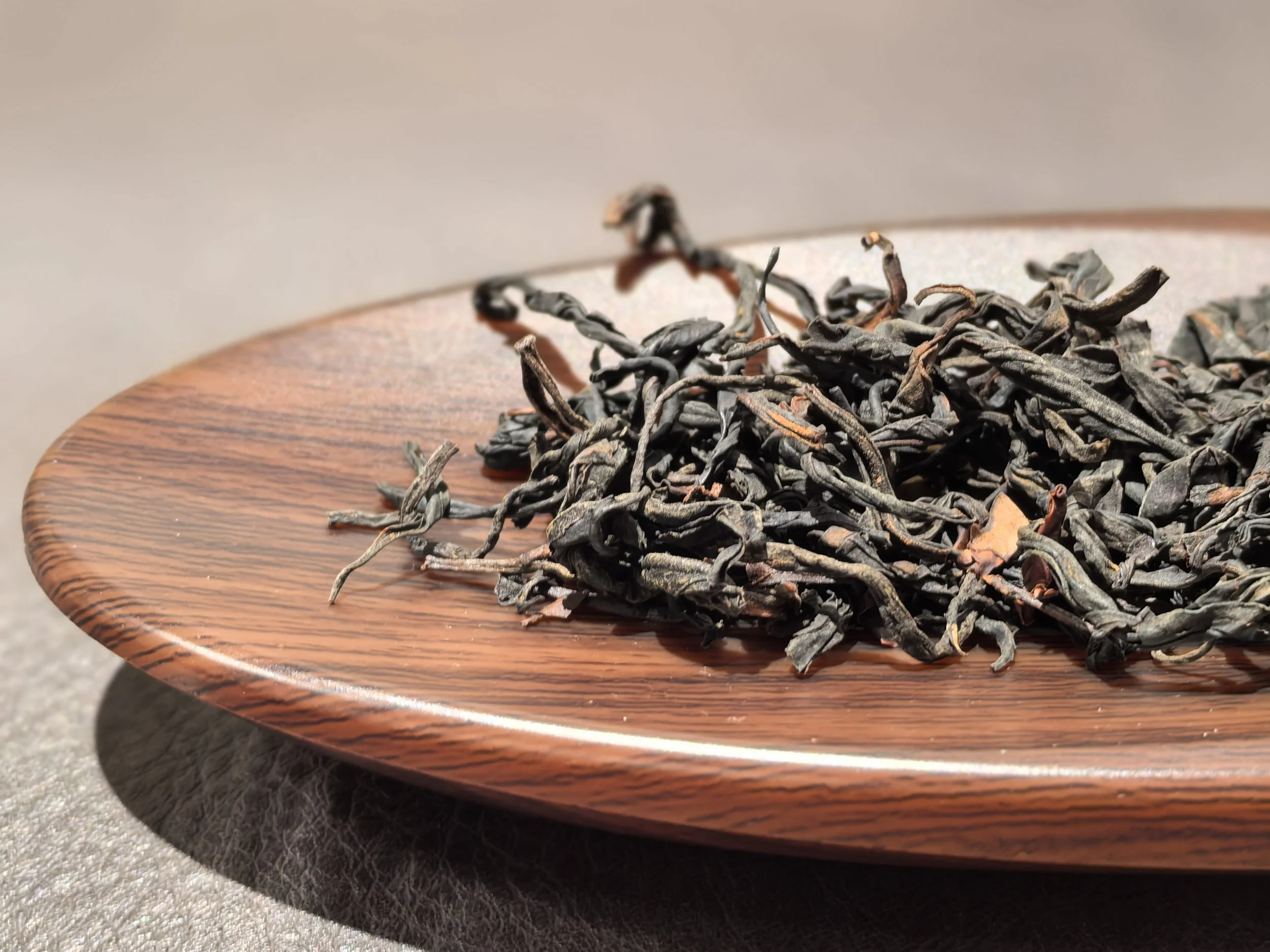 Dried black tea leaves on a round wooden plate.
