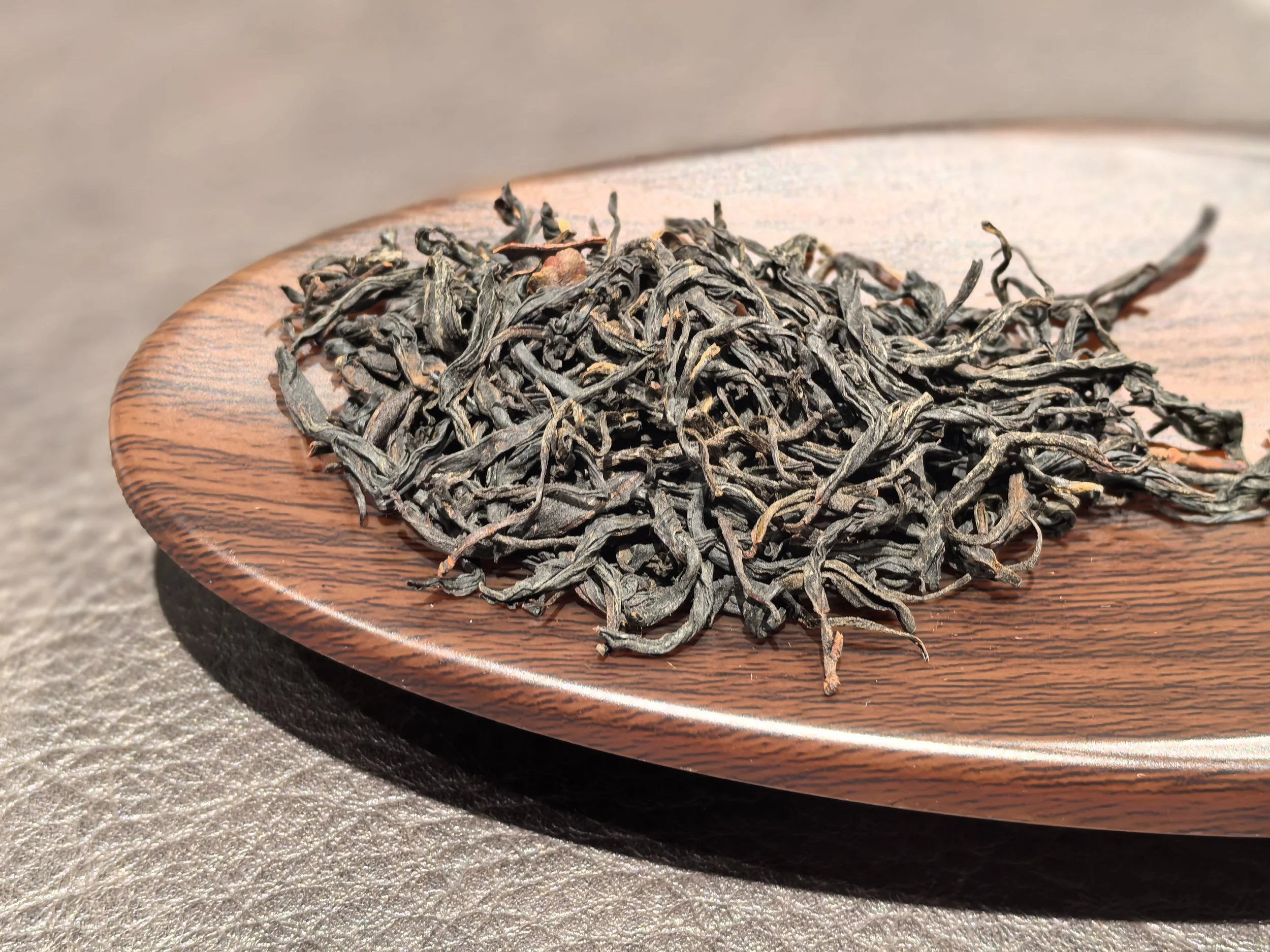 Dried loose black tea leaves on a round wooden plate.