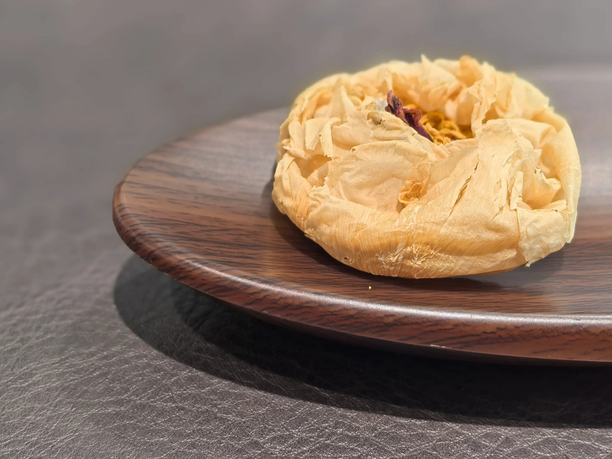 A dried King Peony on a wooden plate.