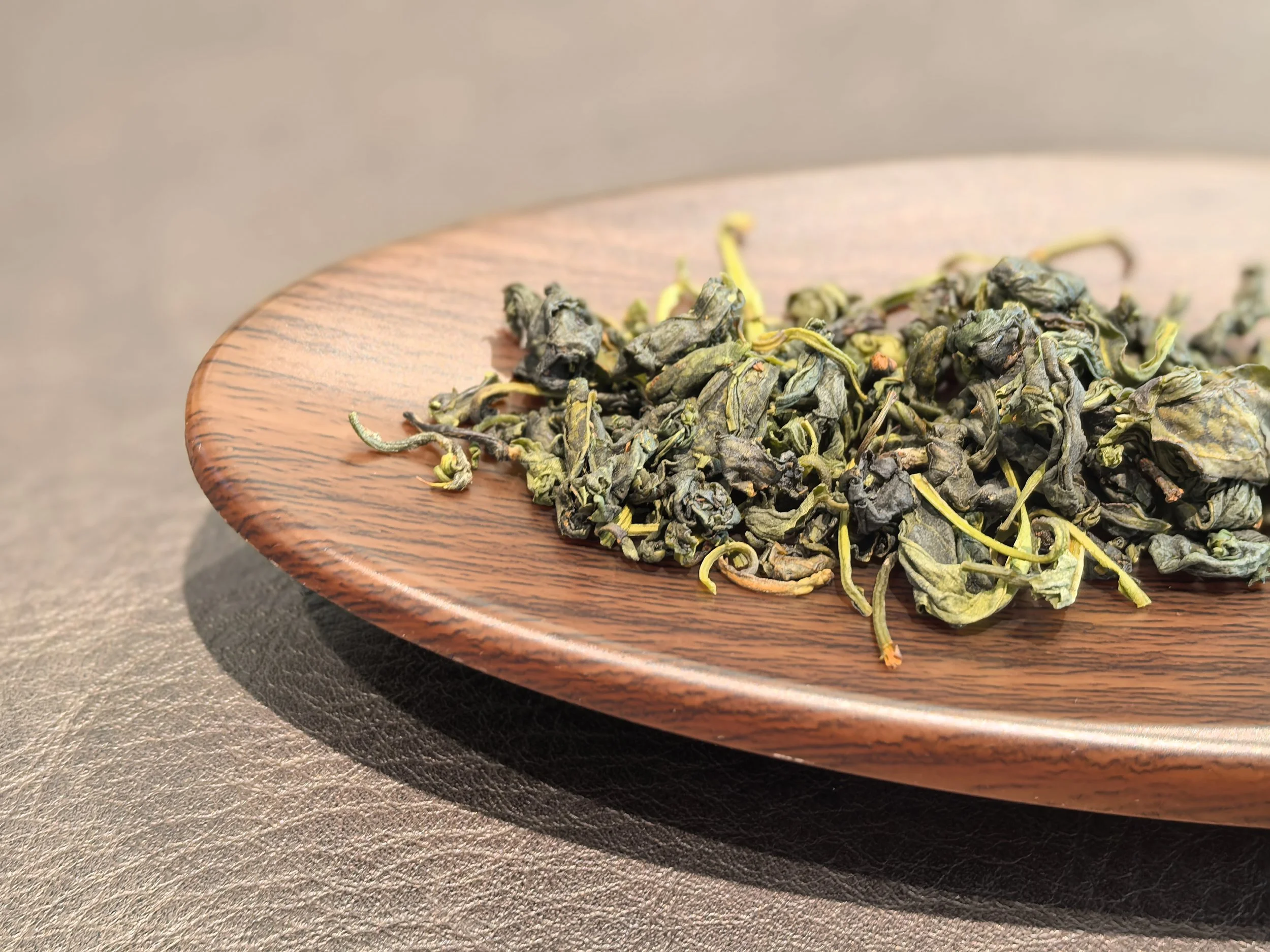 Dried green tea leaves on a wooden plate.