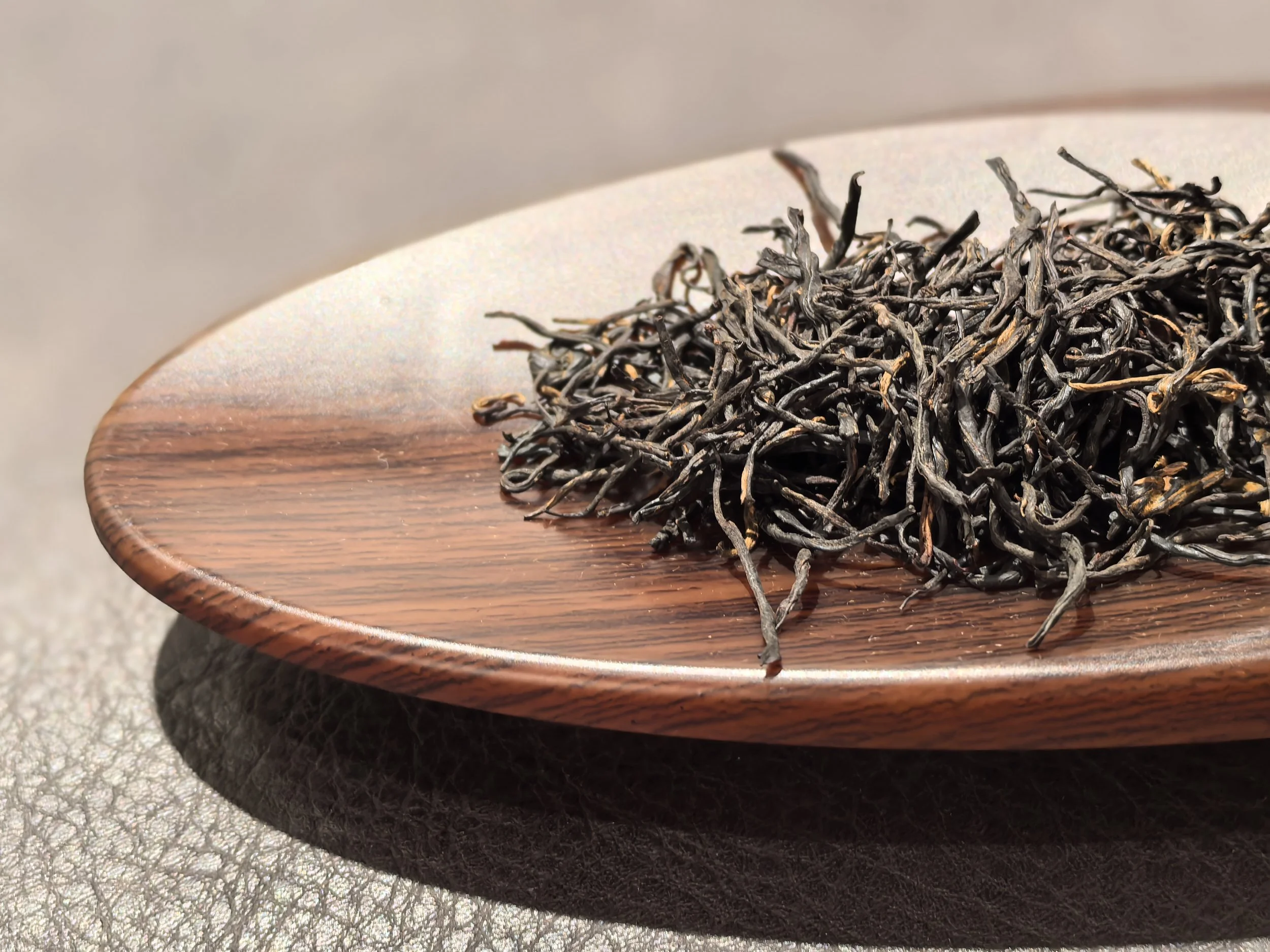 Dried black tea leaves on a wooden plate.