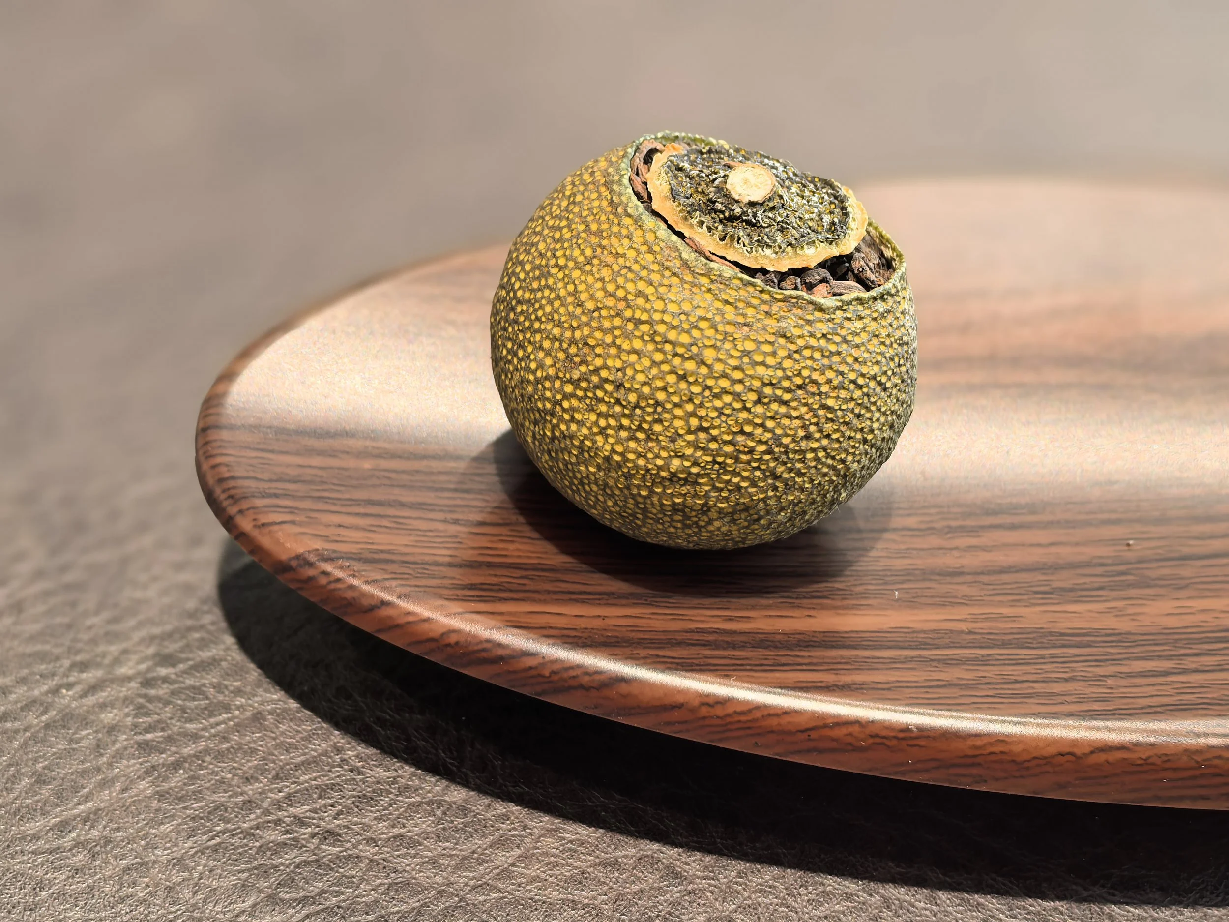 Mini Green Mandarin Puerh Tea gourd with a round shape, cut open at the top, sitting on a wooden plate.