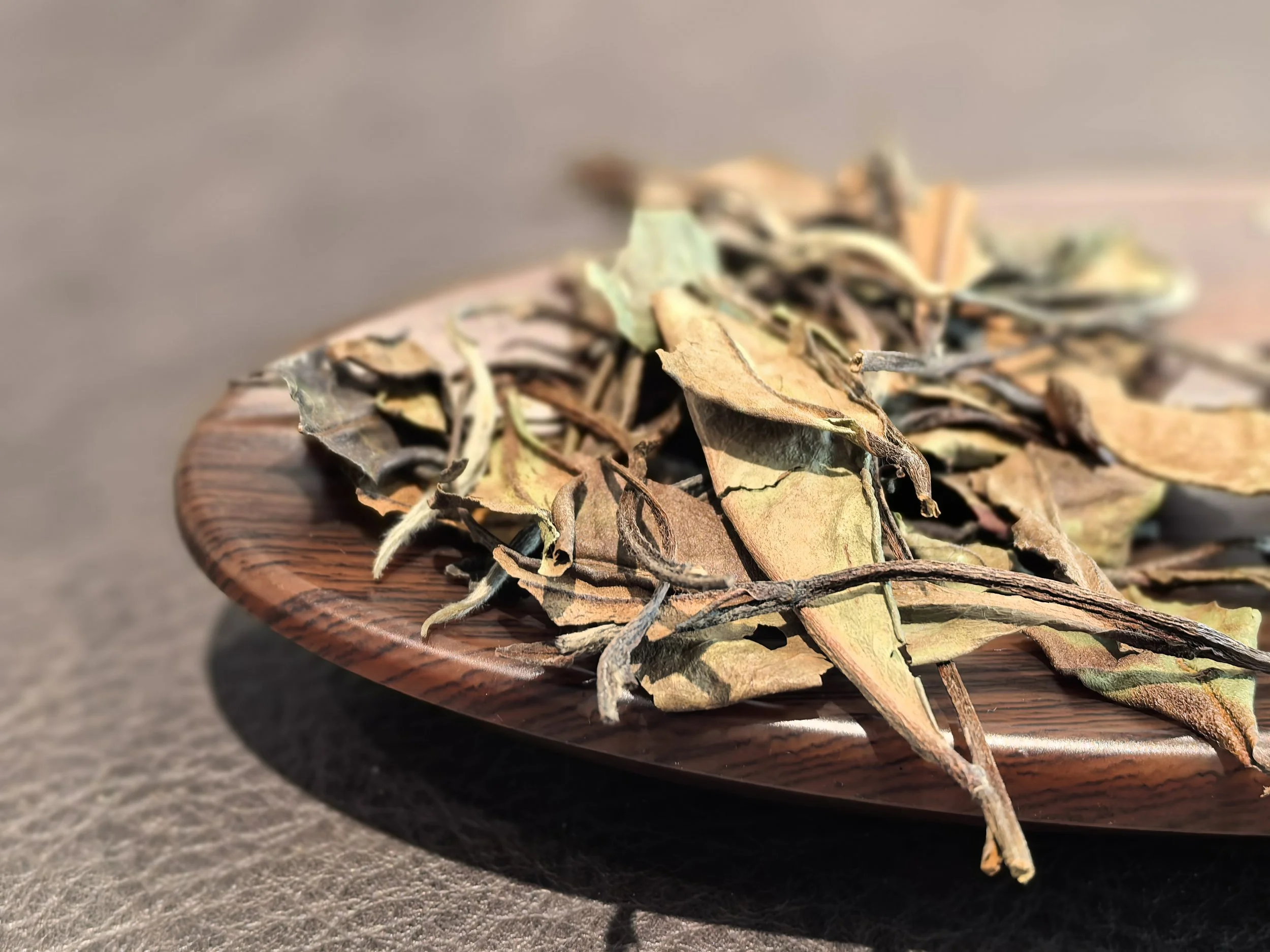 Dried tea leaves and twigs on a wooden plate.