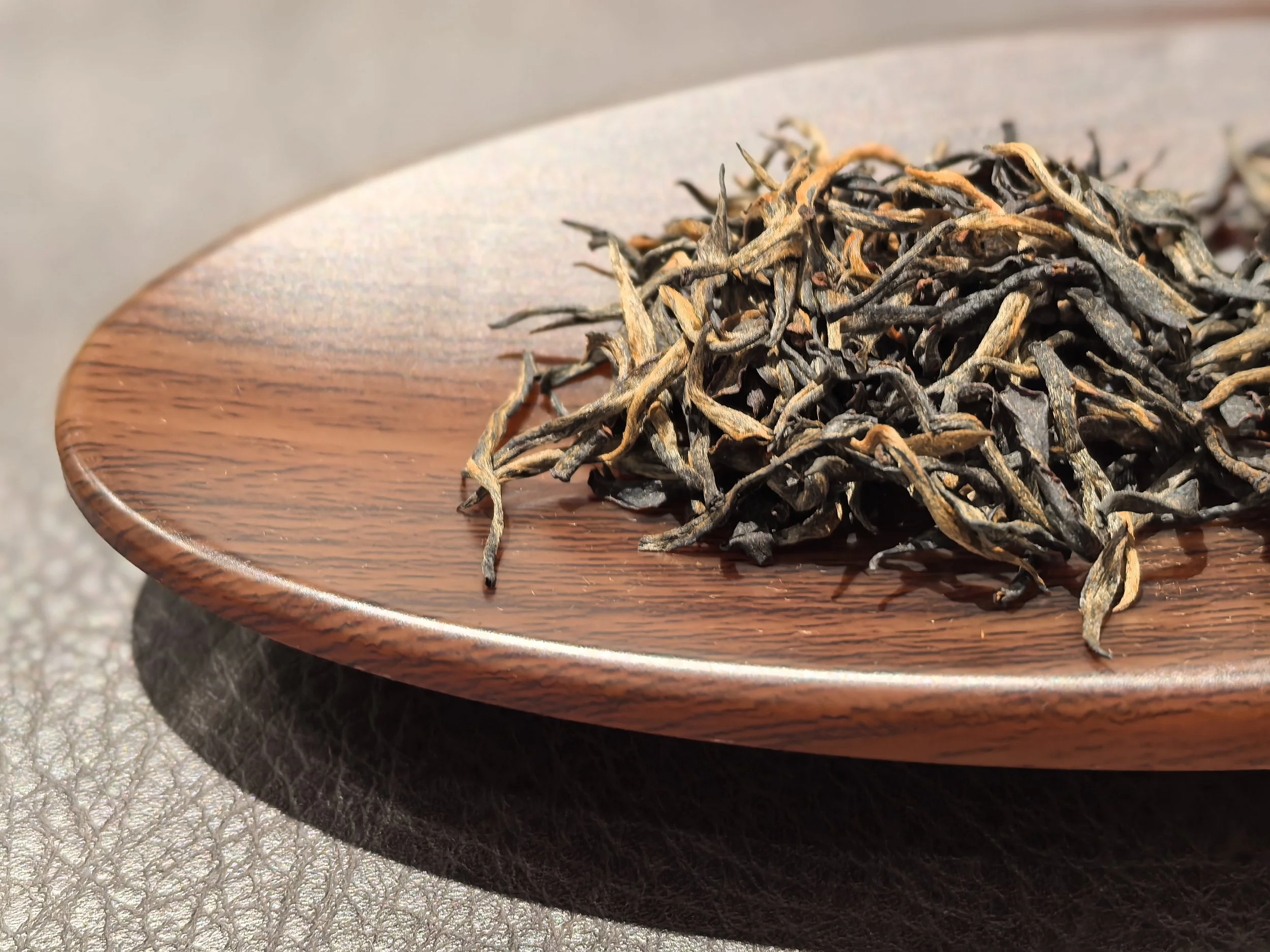 Dried loose black tea leaves on a round wooden plate.