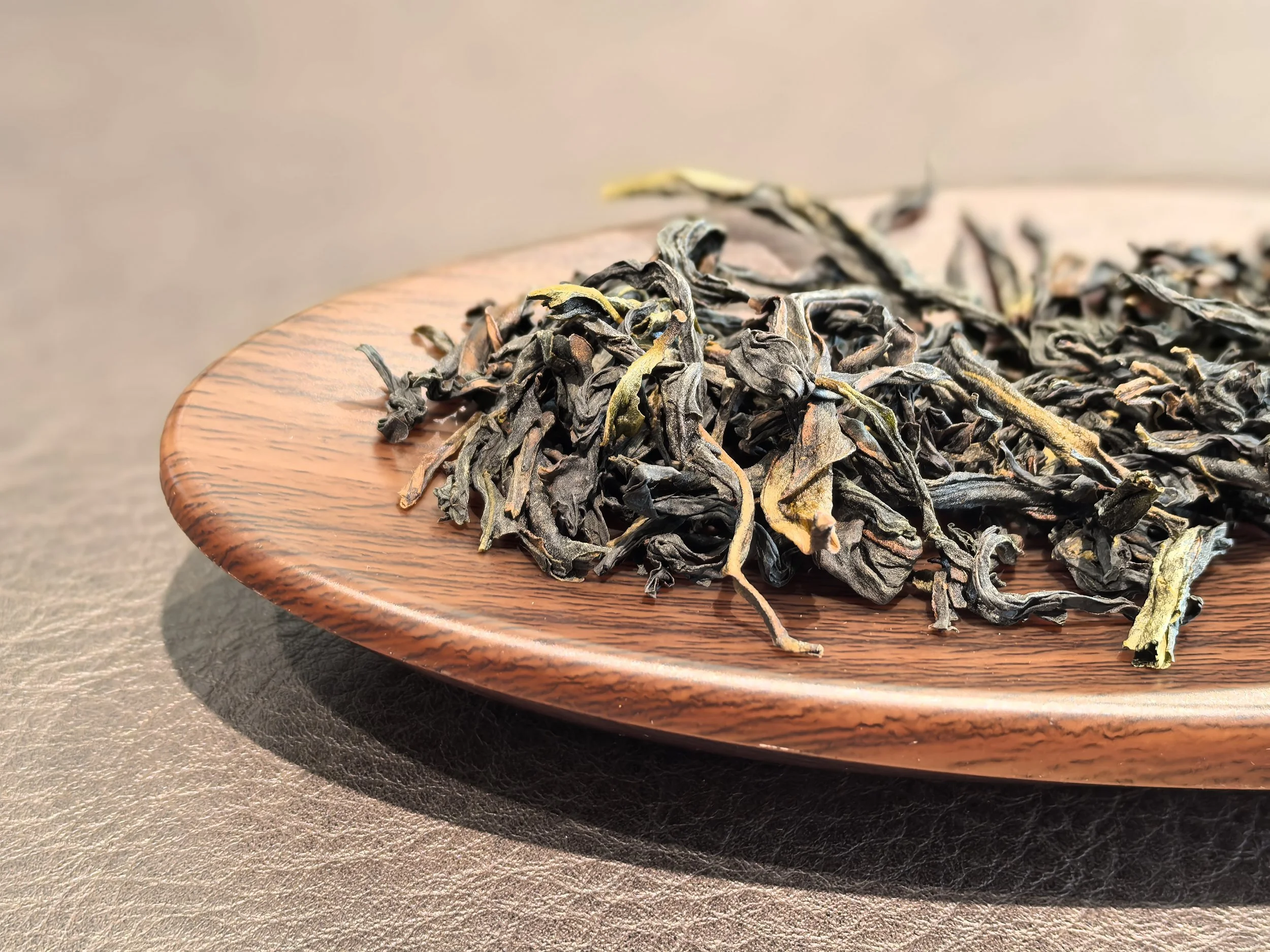 Dried loose tea leaves on a round wooden plate.