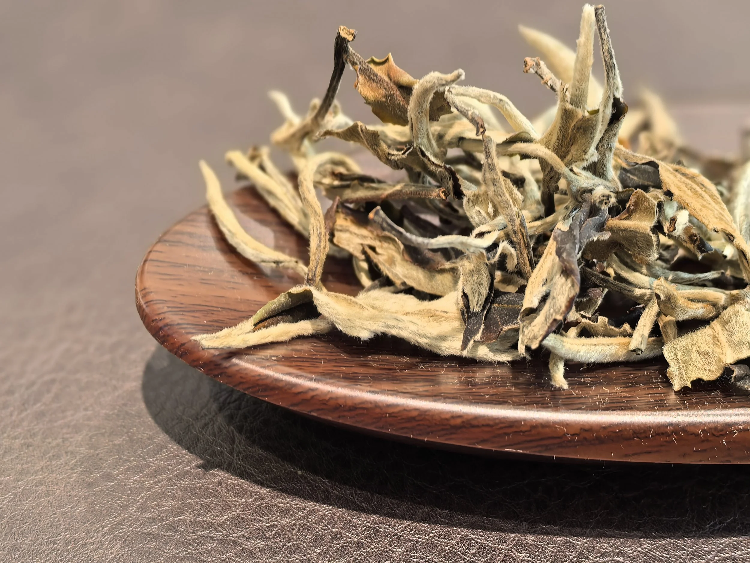 Dried tea leaves on a wooden dish with a neutral background.