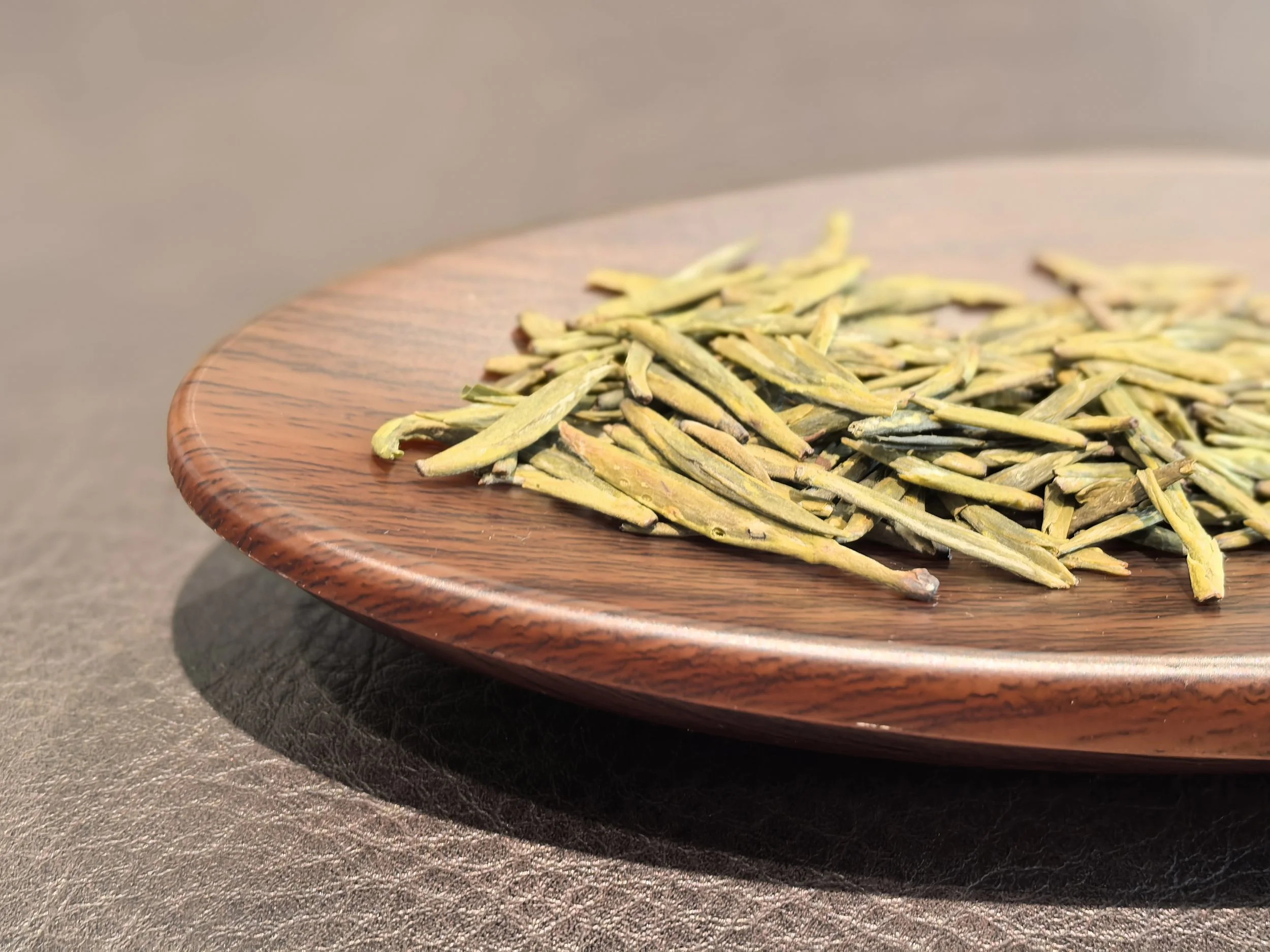 Dried green tea leaves on a wooden plate.