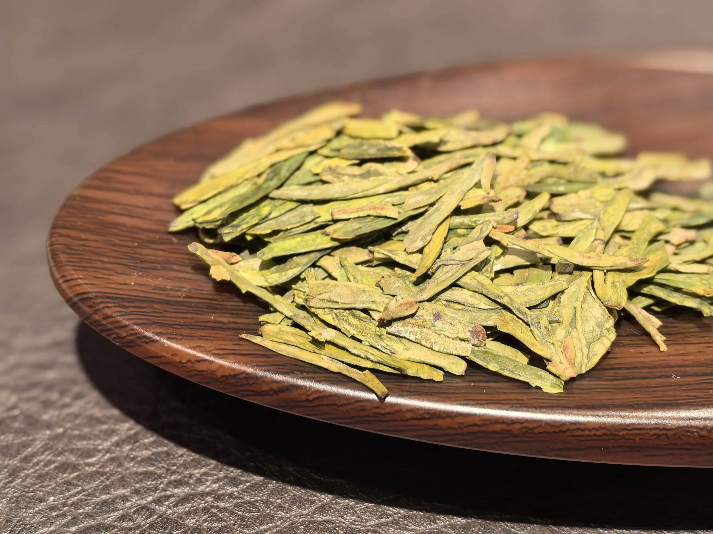Dried green tea leaves on a wooden plate.