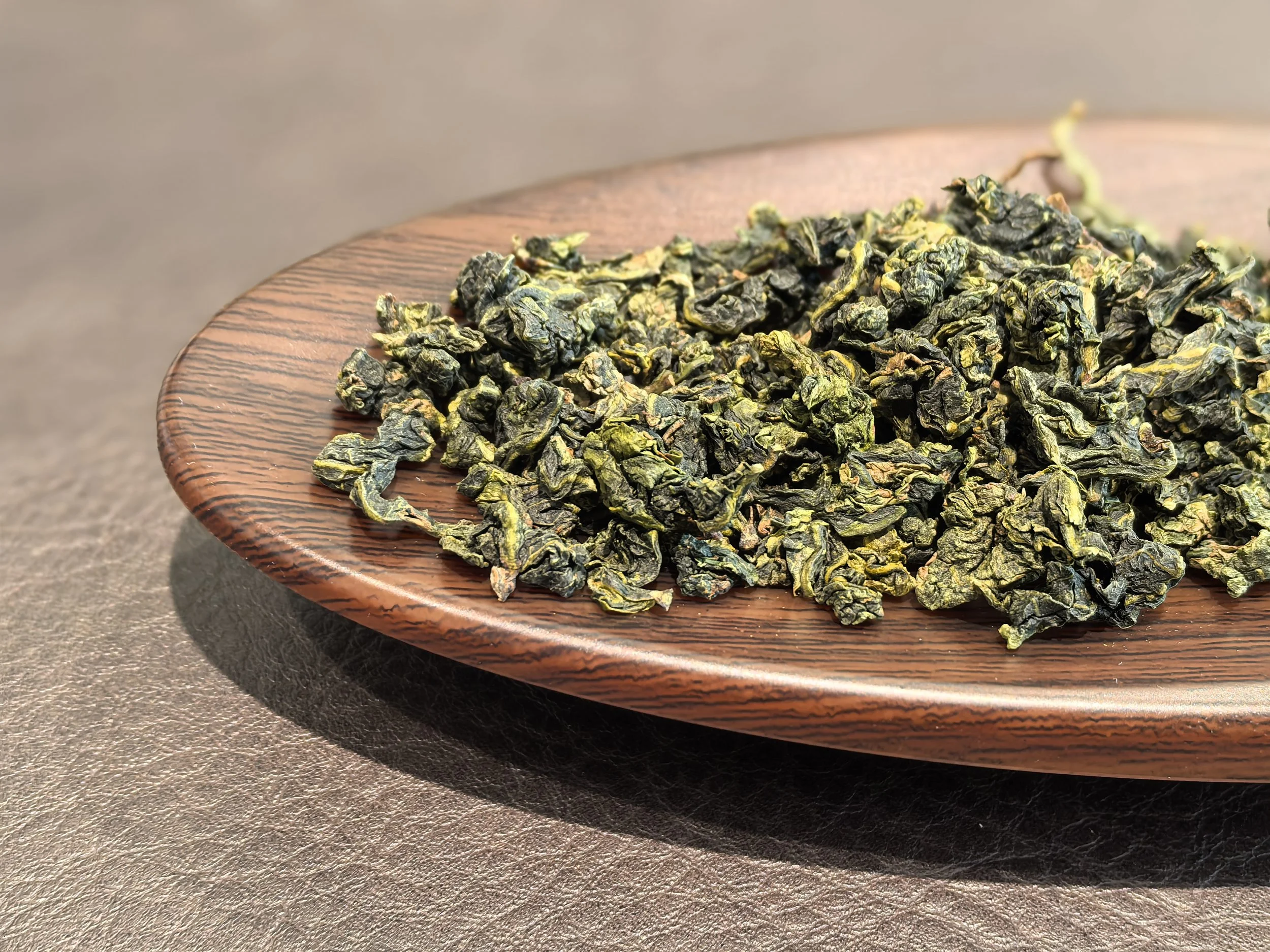 Dried green tea leaves on a round wooden plate.