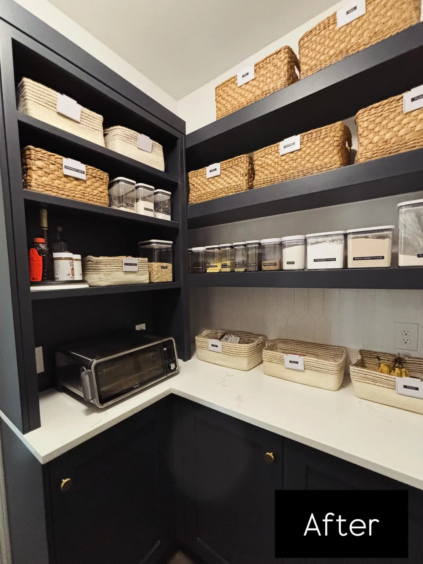 The most beautiful pantry still benefitted from categorization. A breakfast station with peanut butters and honeys on a turntable, basket of oatmeal packets, and pancake mix above the toaster oven. A basket with assorted breads and fruits are in the 
