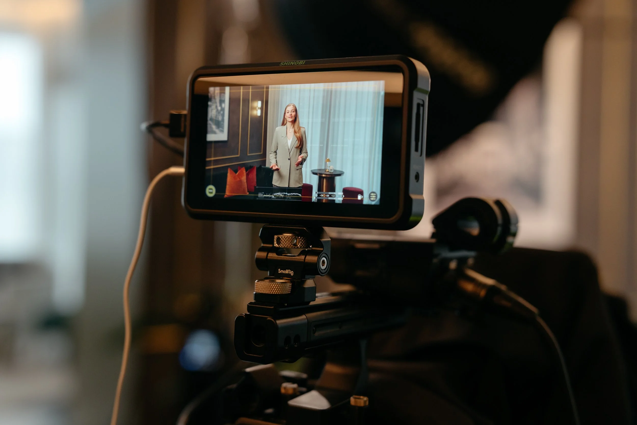A close up photo of a monitor on a camera, showing a woman on set, talking to the camera.
