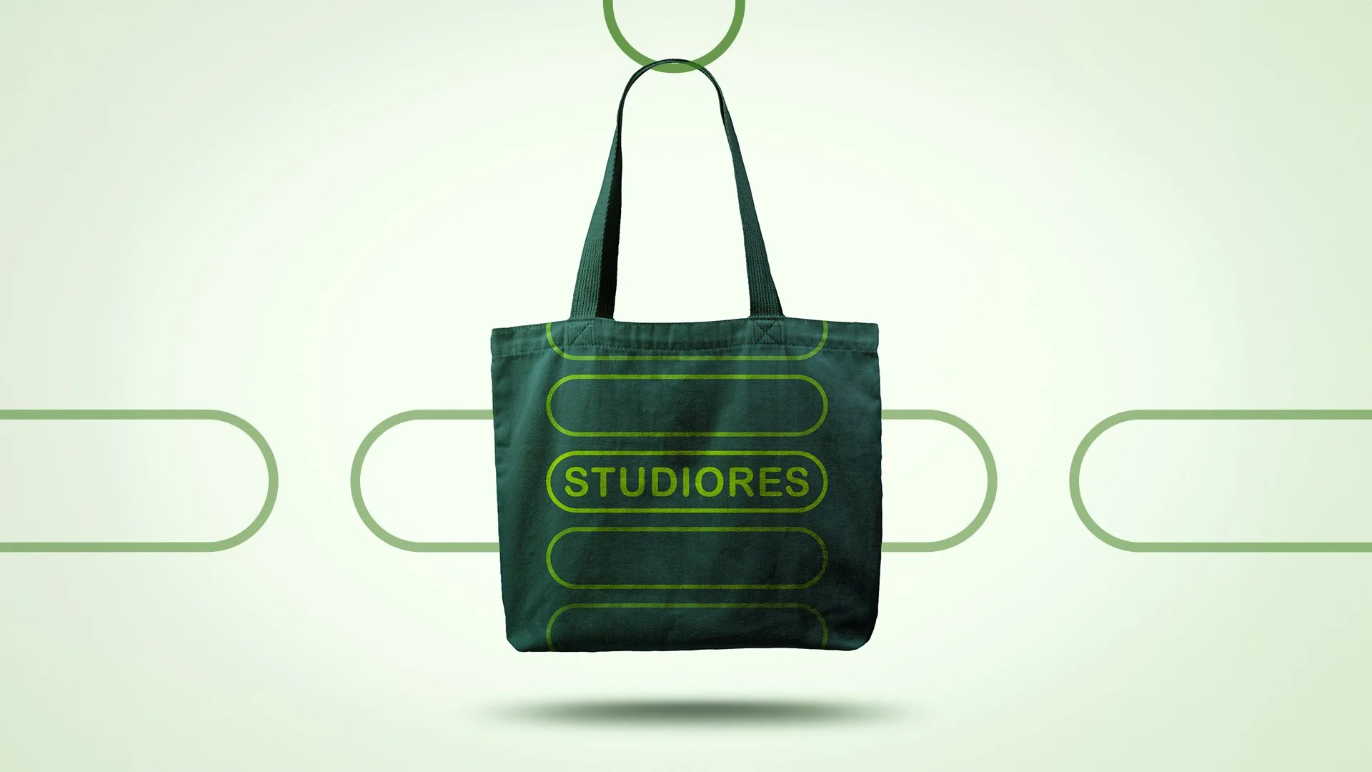 Green tote bag hanging from a hook with the word 'STUDIORES' printed on it, set against a light green background with a pattern of connecting lines.