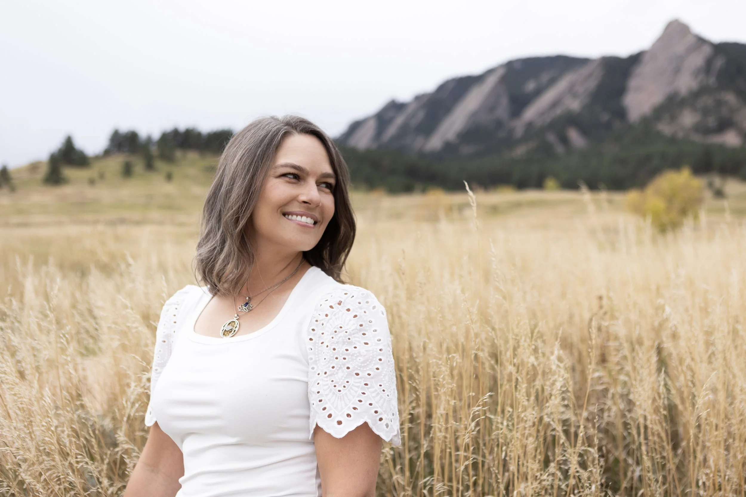 Woman in the foreground with a grassy field in the middleground and mountains in the background