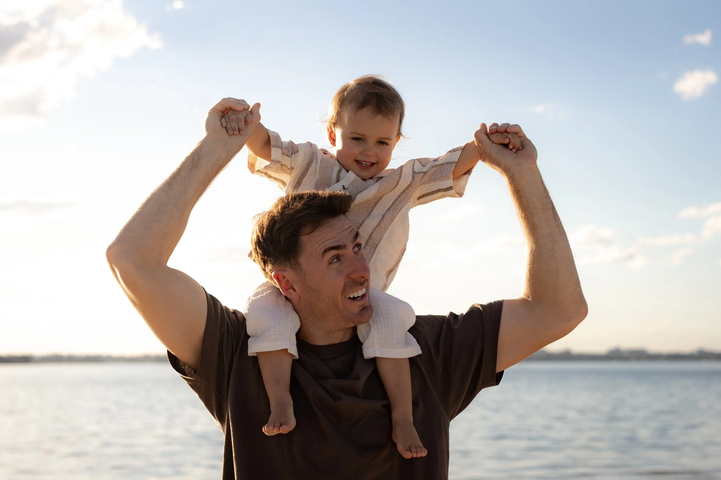 Father lifting his young son onto his shoulders during a playful Christmas Minis family beach photoshoot in Kurnell.