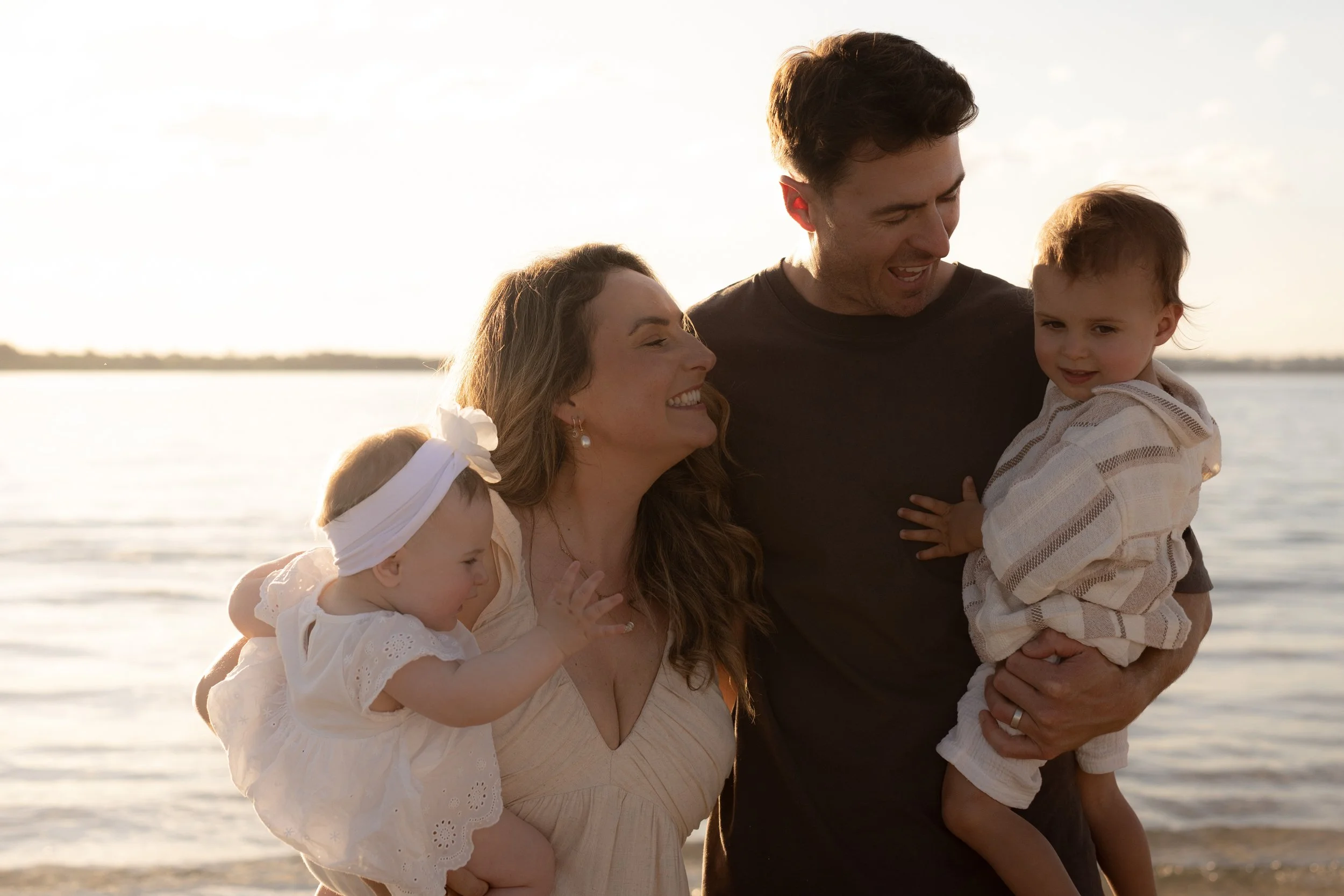Parents sharing a joyful moment with their two young children during a golden hour family beach photoshoot.