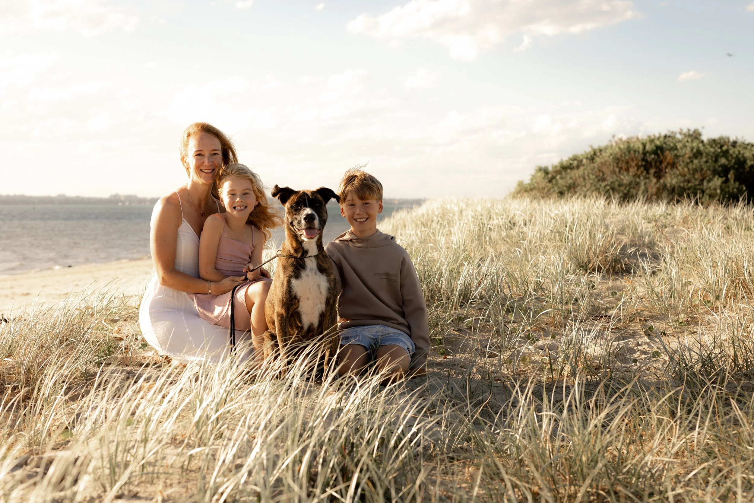 Mother and two children sitting with their family dog among the beach grass during a Christmas mini session in Kurnell.