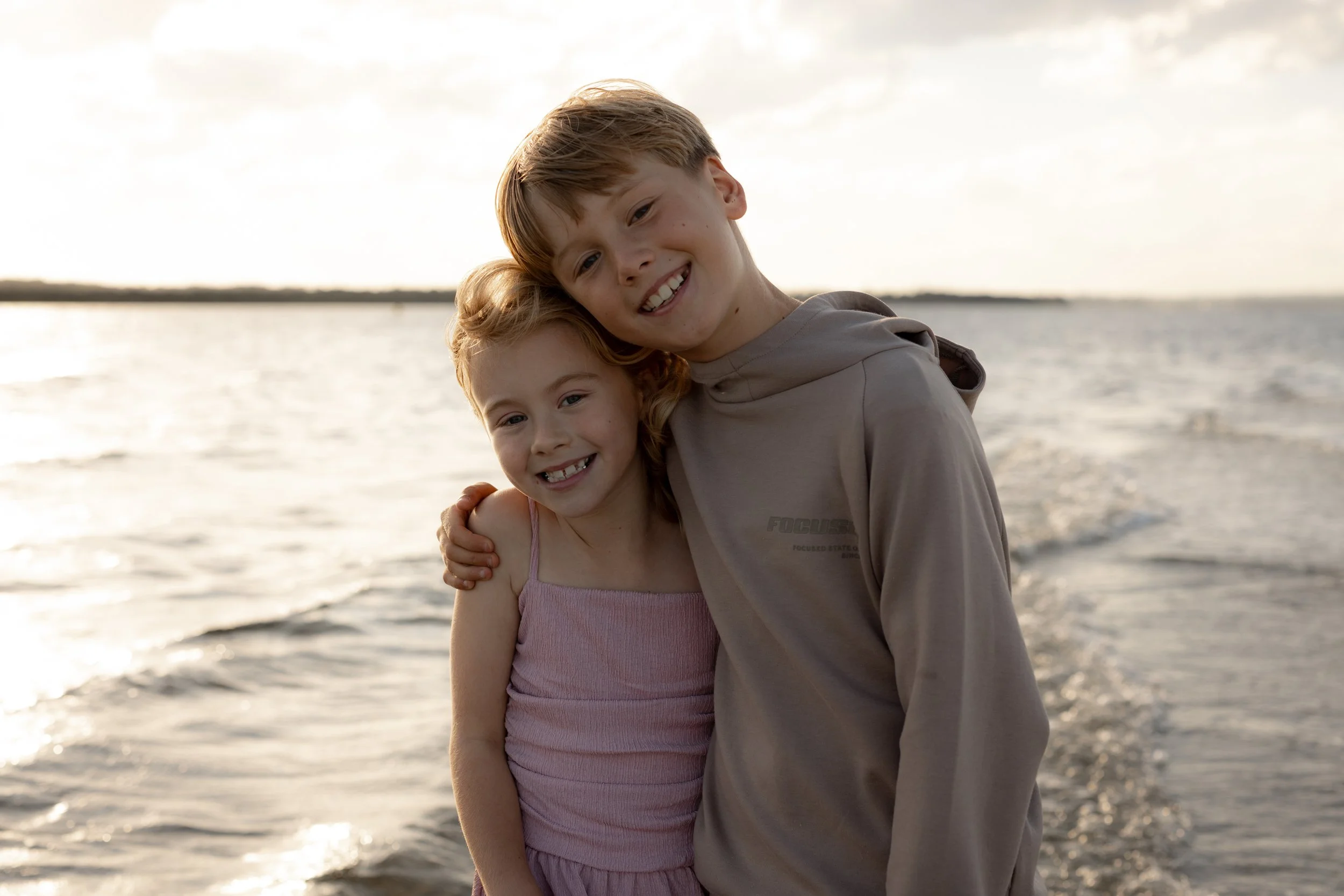A brother and sister embracing whilst standing in the shallow waters just before sunset.