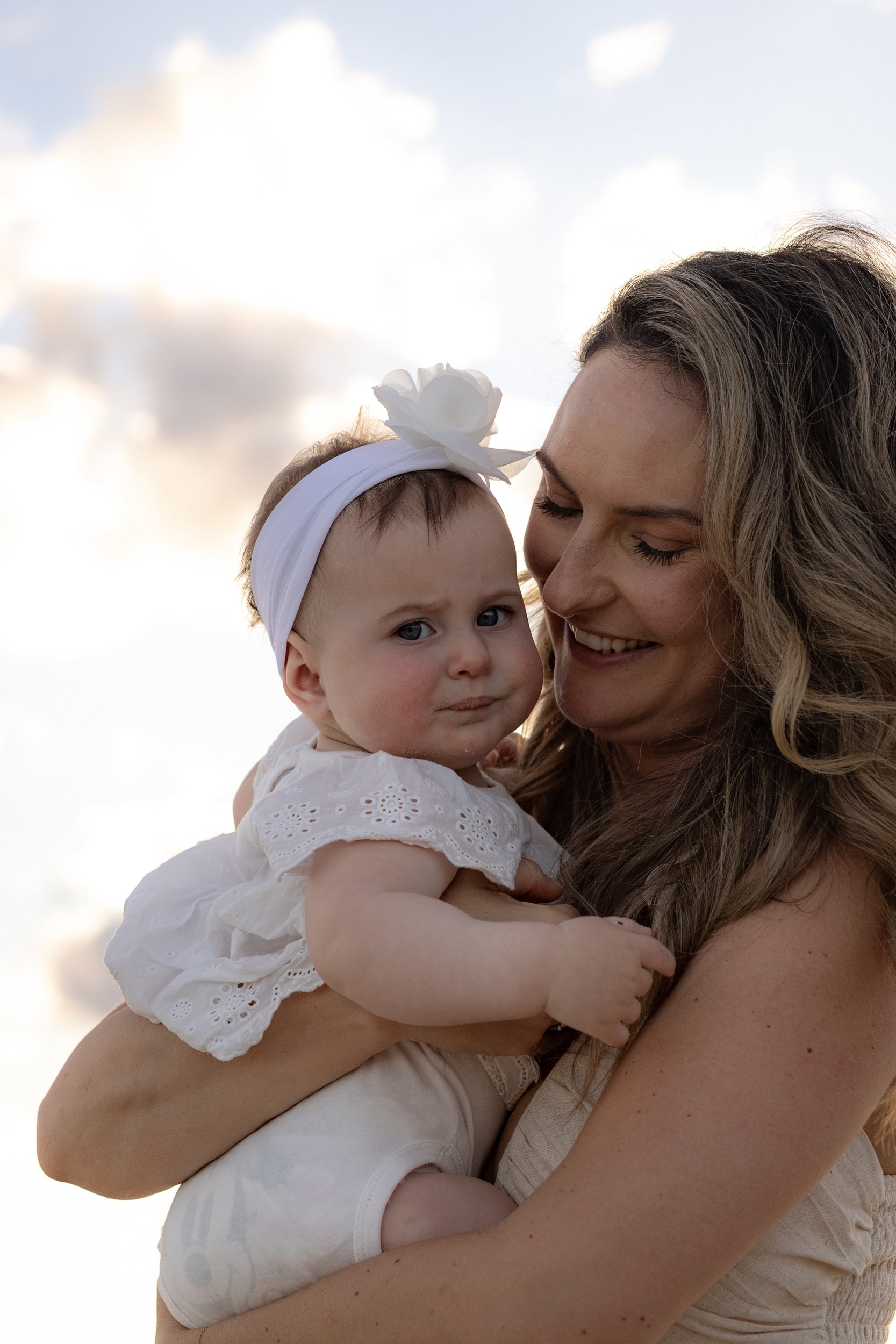Mother cuddling her baby daughter in a natural sunset family portrait on the beach in Sydney.