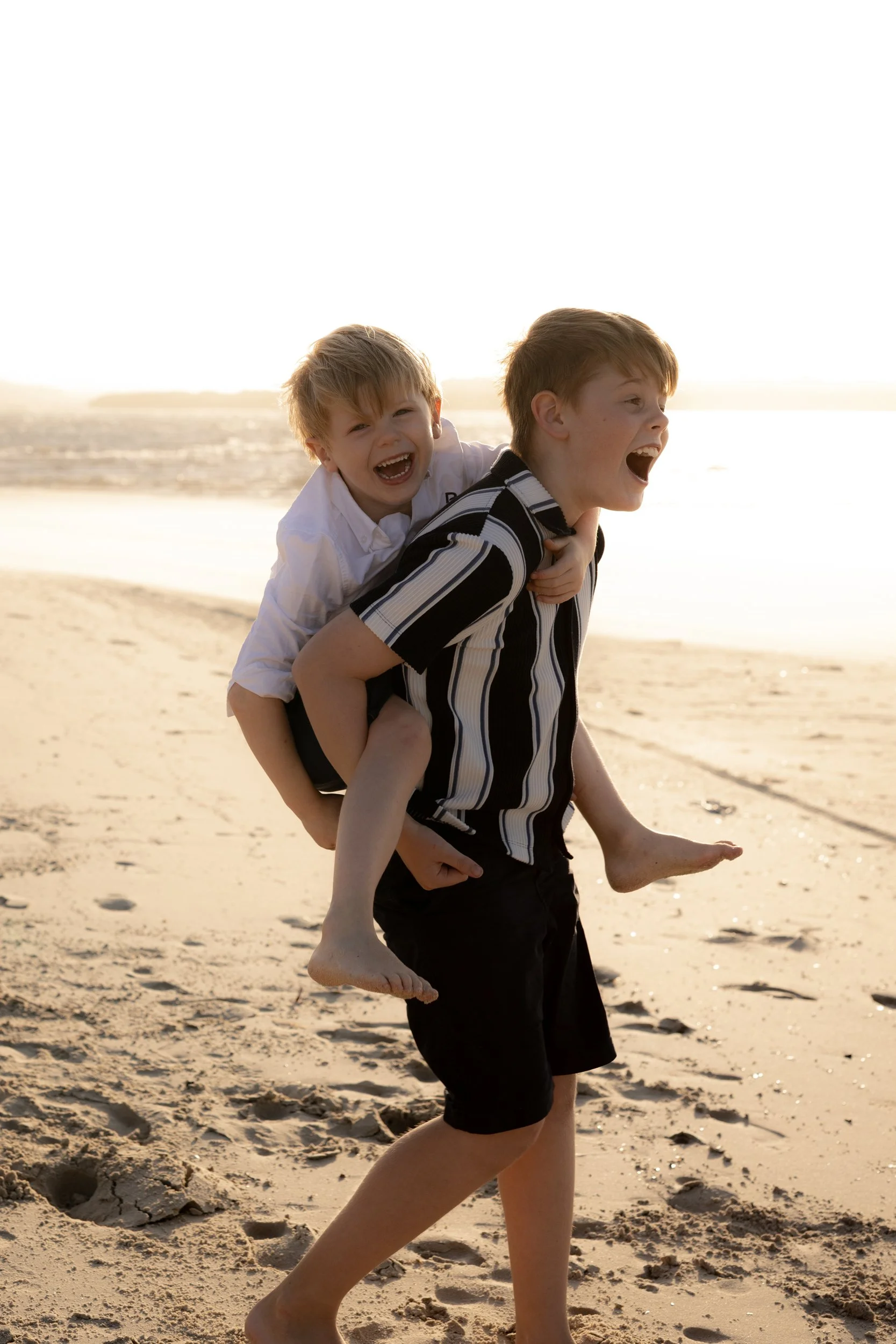 Two brothers laughing and playing together during a playful family beach photoshoot in the Sutherland Shire.
