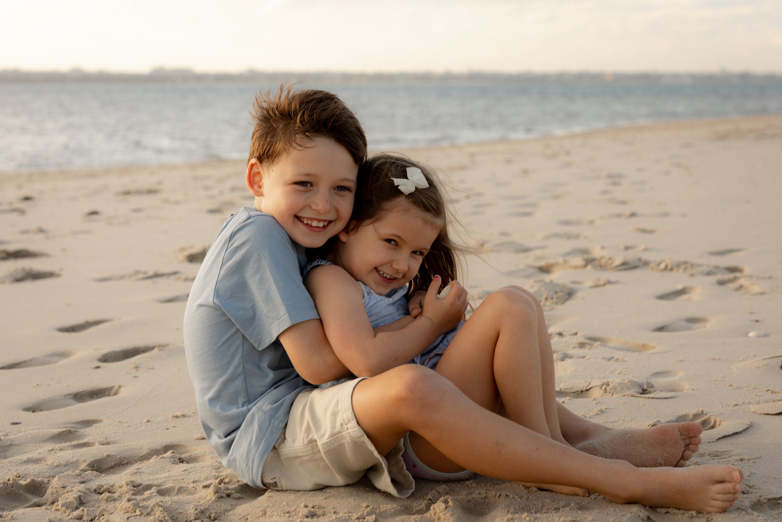 Two siblings cuddling together on the beach during a Christmas mini family photography session in Kurnell.