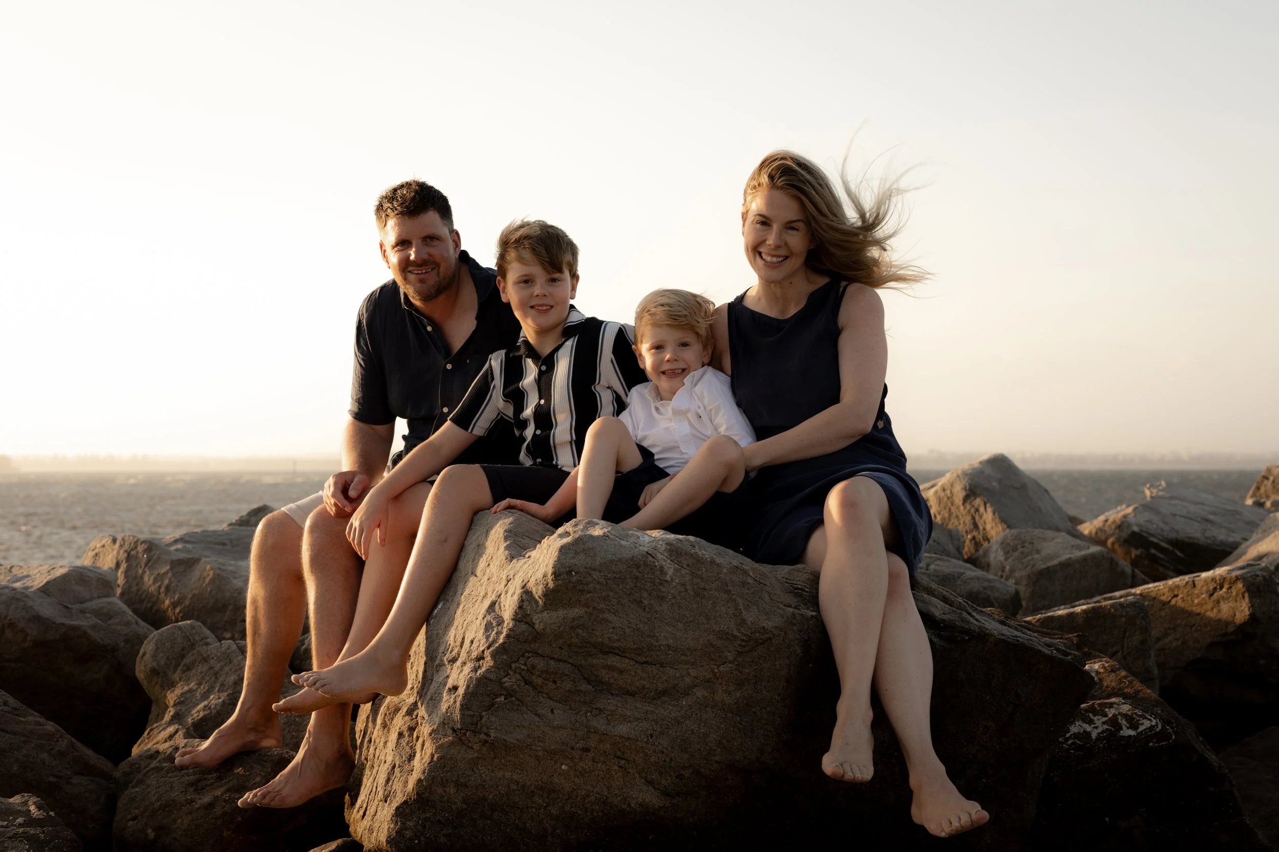 Family of four sitting together on the rocks by the water during a sunset family photography session near Cronulla.