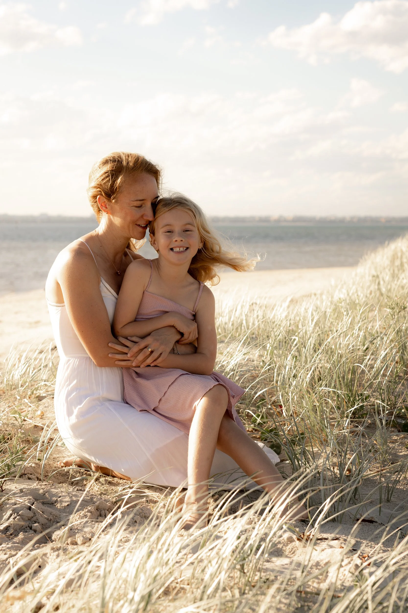 Mother cuddling her young daughter in the coastal grass during a golden hour family portrait at Kurnell beach.
