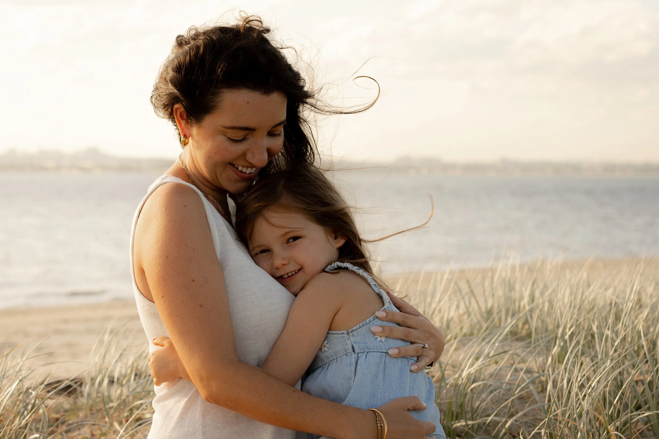 Mother cuddling her young daughter on Kurnell beach at sunset during a Christmas mini family photo session.