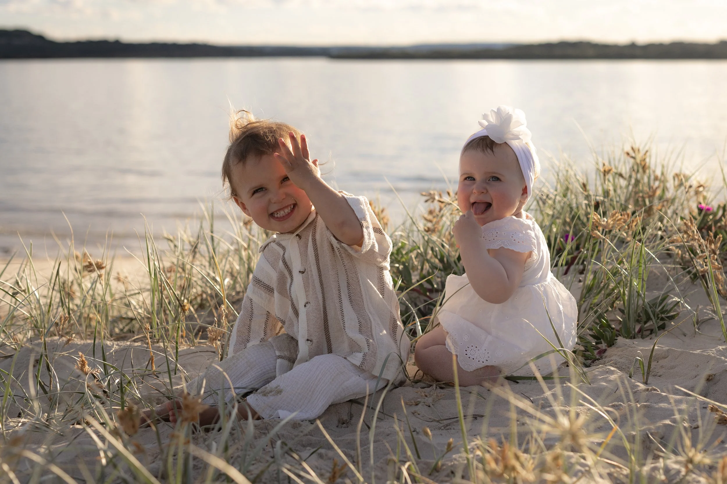 Two little siblings smiling and playing together in the beach grass during a natural family photoshoot in Kurnell.