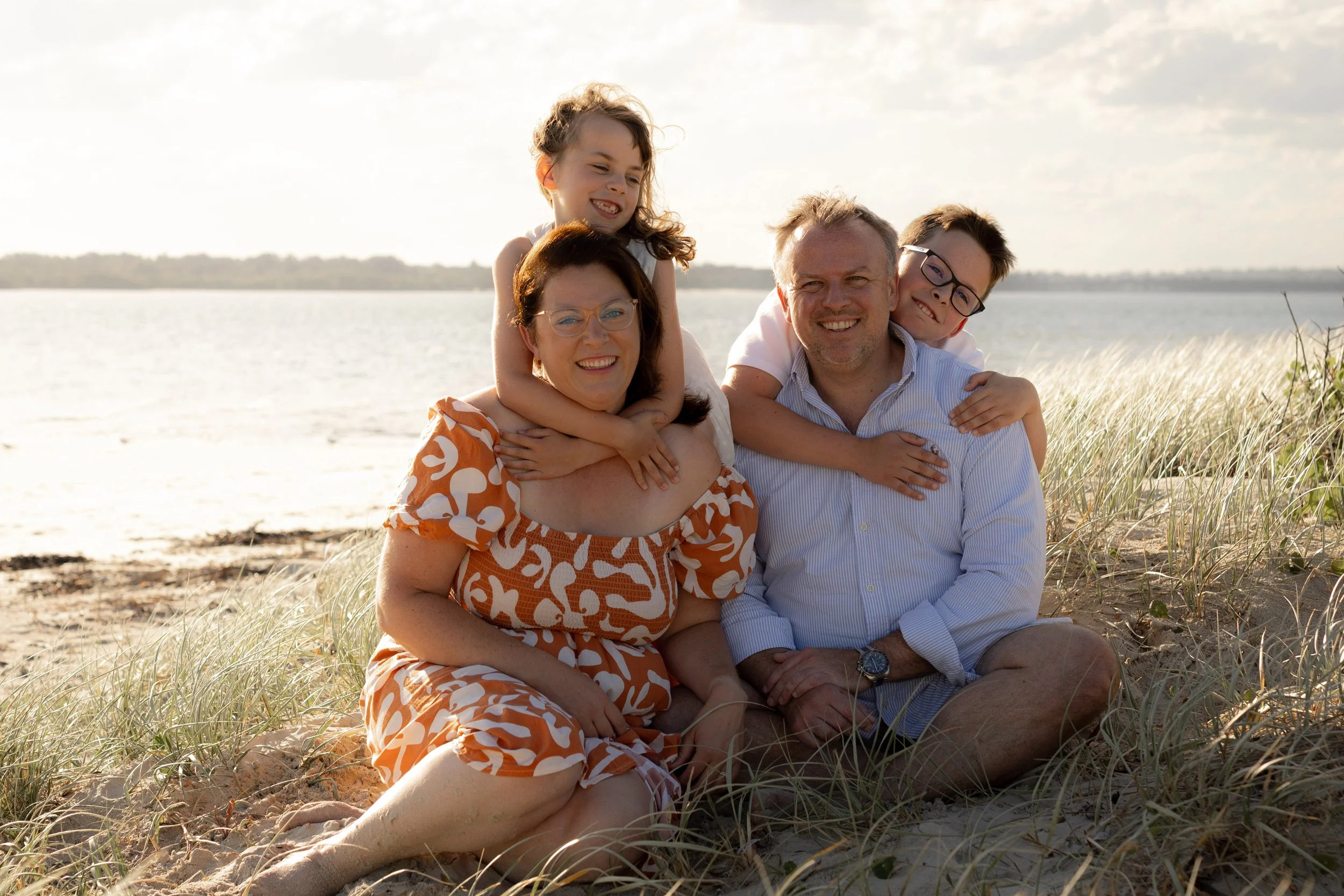 Family of four sitting together in the sand dunes during a relaxed Christmas mini photoshoot in Kurnell.