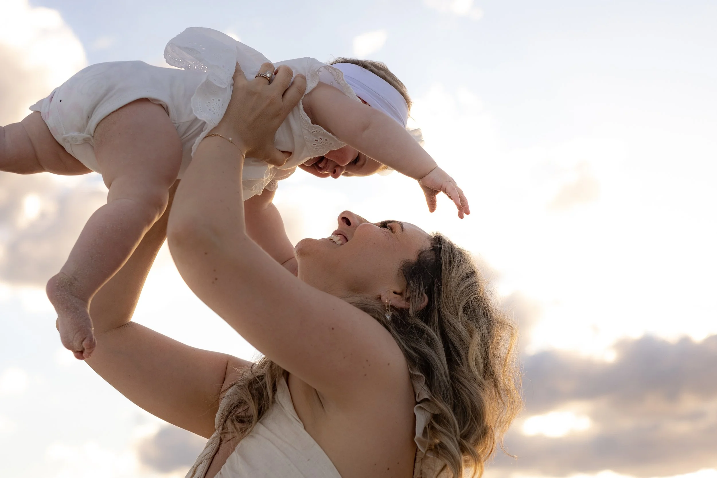 Mum lifting her baby daughter into the air on the beach during a golden hour family photoshoot in Kurnell.