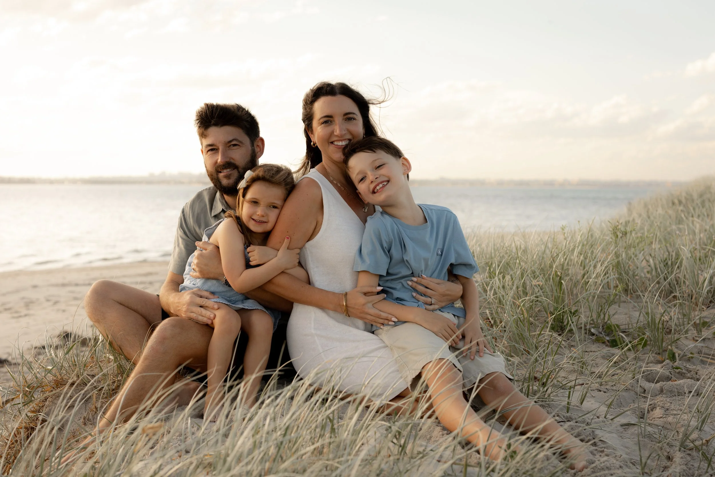 Parents cuddling their two children on the beach during a relaxed sunset Christmas mini photo session.
