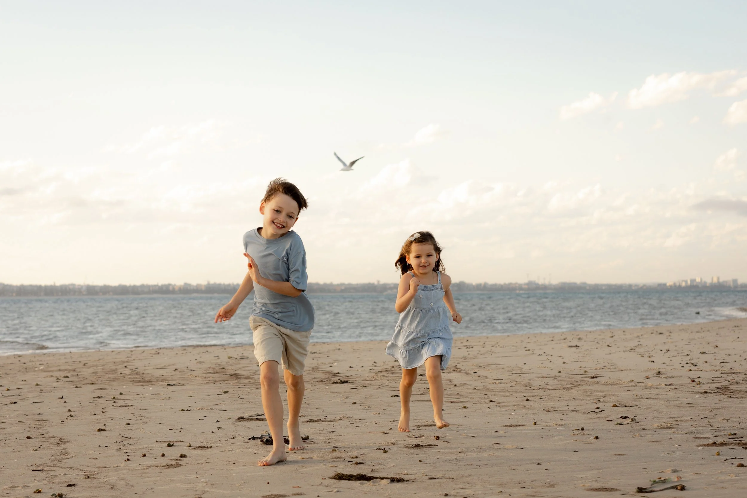 Two young siblings running along the sand together during a relaxed beach family Christmas Minis photoshoot in the Sutherland Shire.