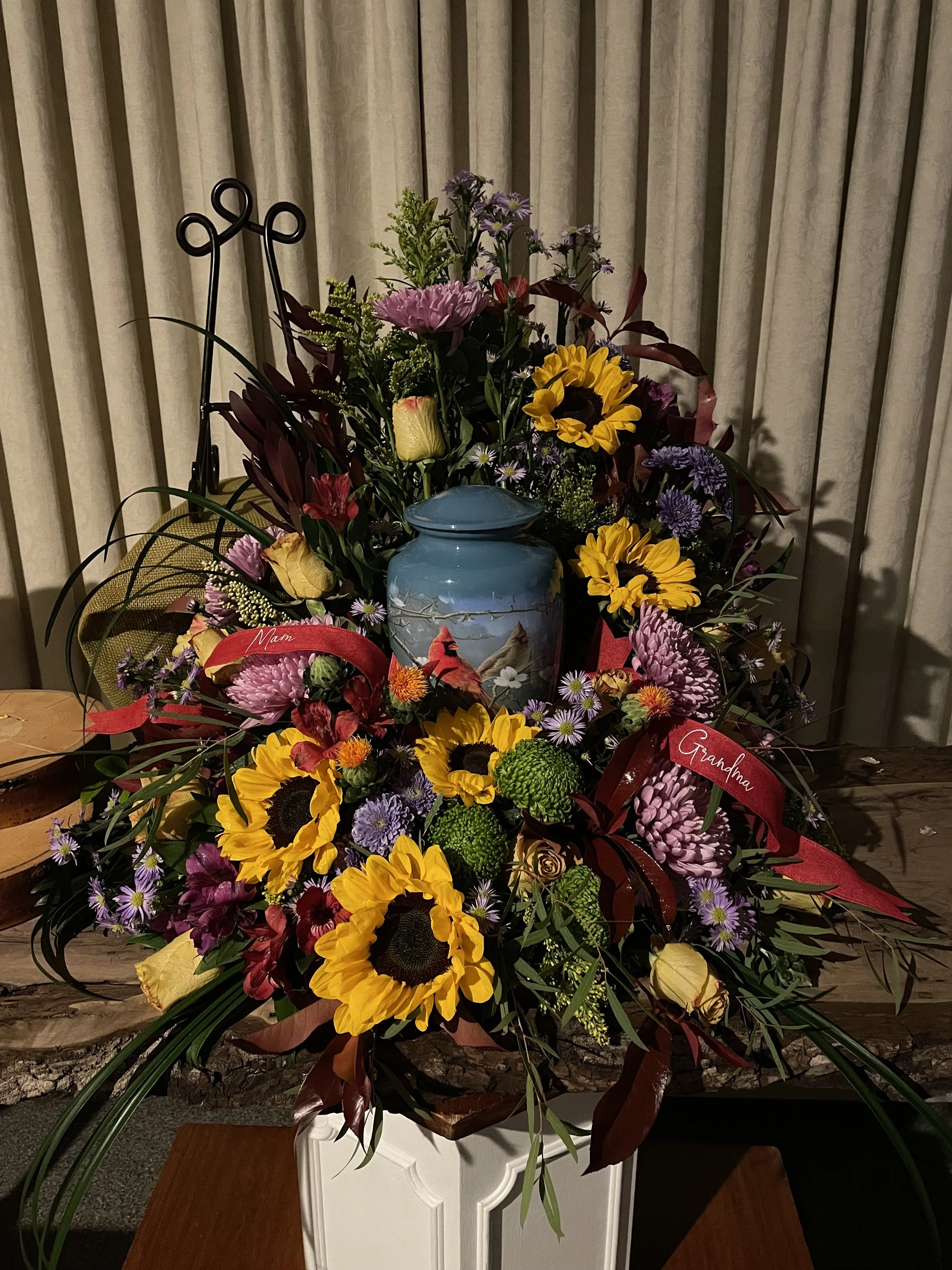 Colorful floral arrangement with sunflowers, purple, yellow, and green flowers in a white vase.
