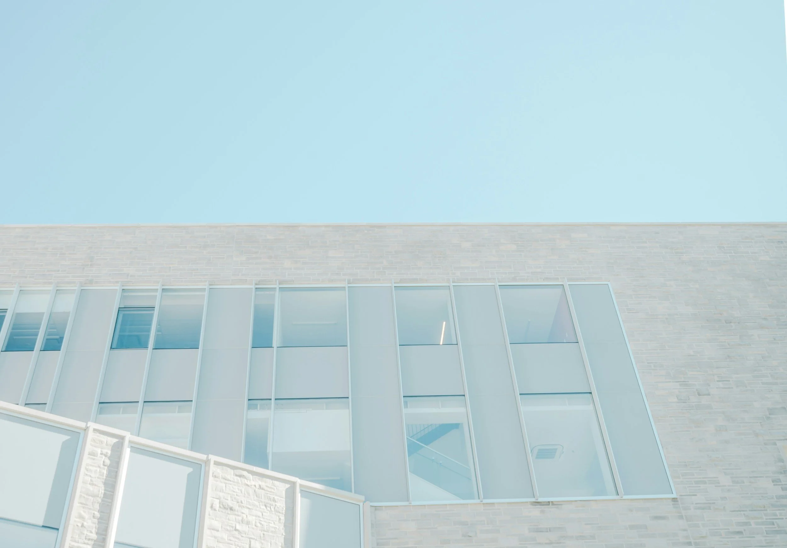 Modern building façade with large glass windows and light brick exterior, under a clear blue sky.