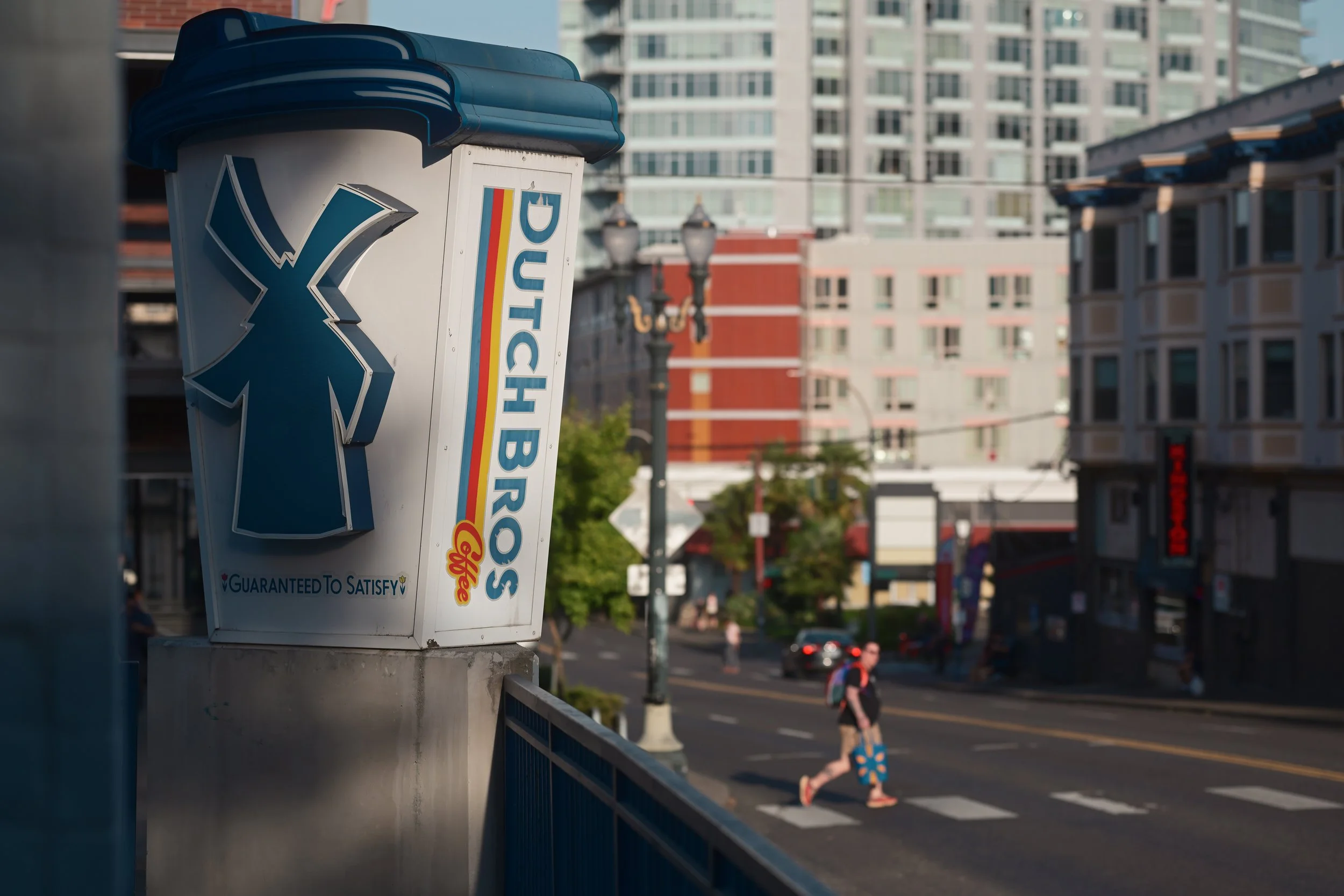 A public telephone booth with a blue roof and white body, displaying the words 'PUBLIC PHONE' with a logo and a tagline 'Guaranteed to Satisfy' on a city street.
