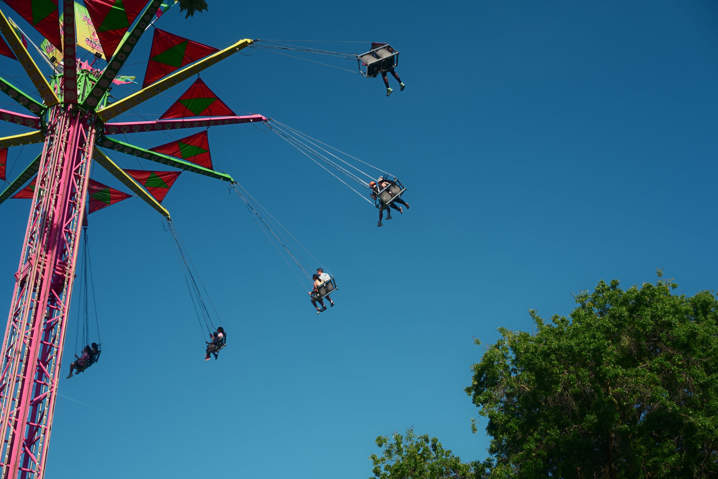 People riding on a colorful Ferris wheel at an amusement park on a clear, sunny day.