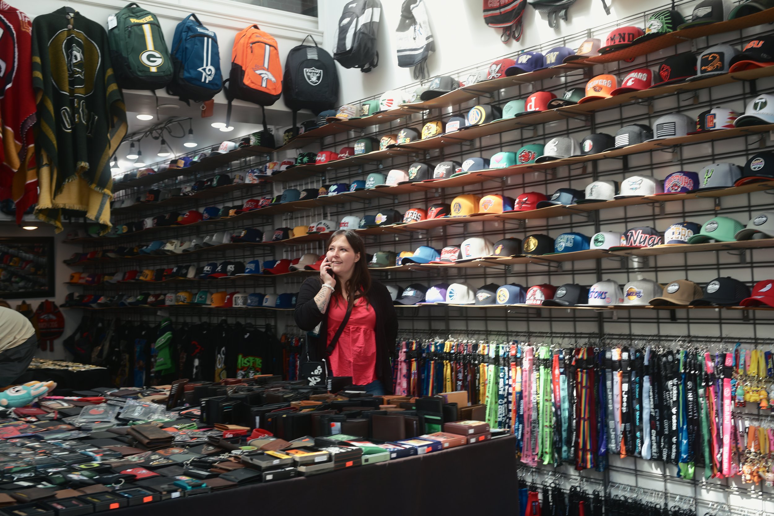 A woman shopping in a store with shelves full of sports caps, backpacks, and various accessories.