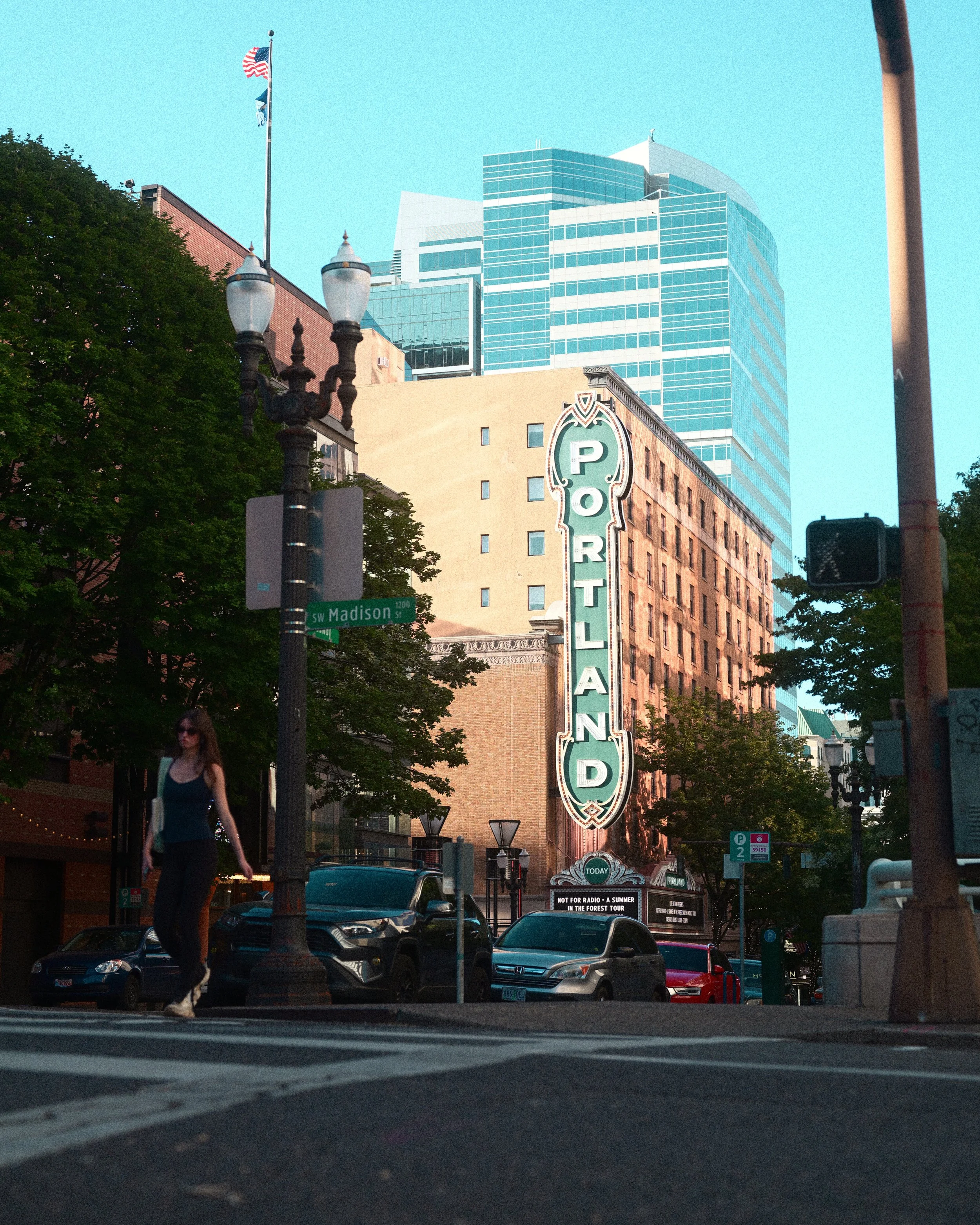 Downtown Portland street scene with the historic Portland marquee, American flag, modern glass buildings, parked cars, and a SW Madison Street sign.