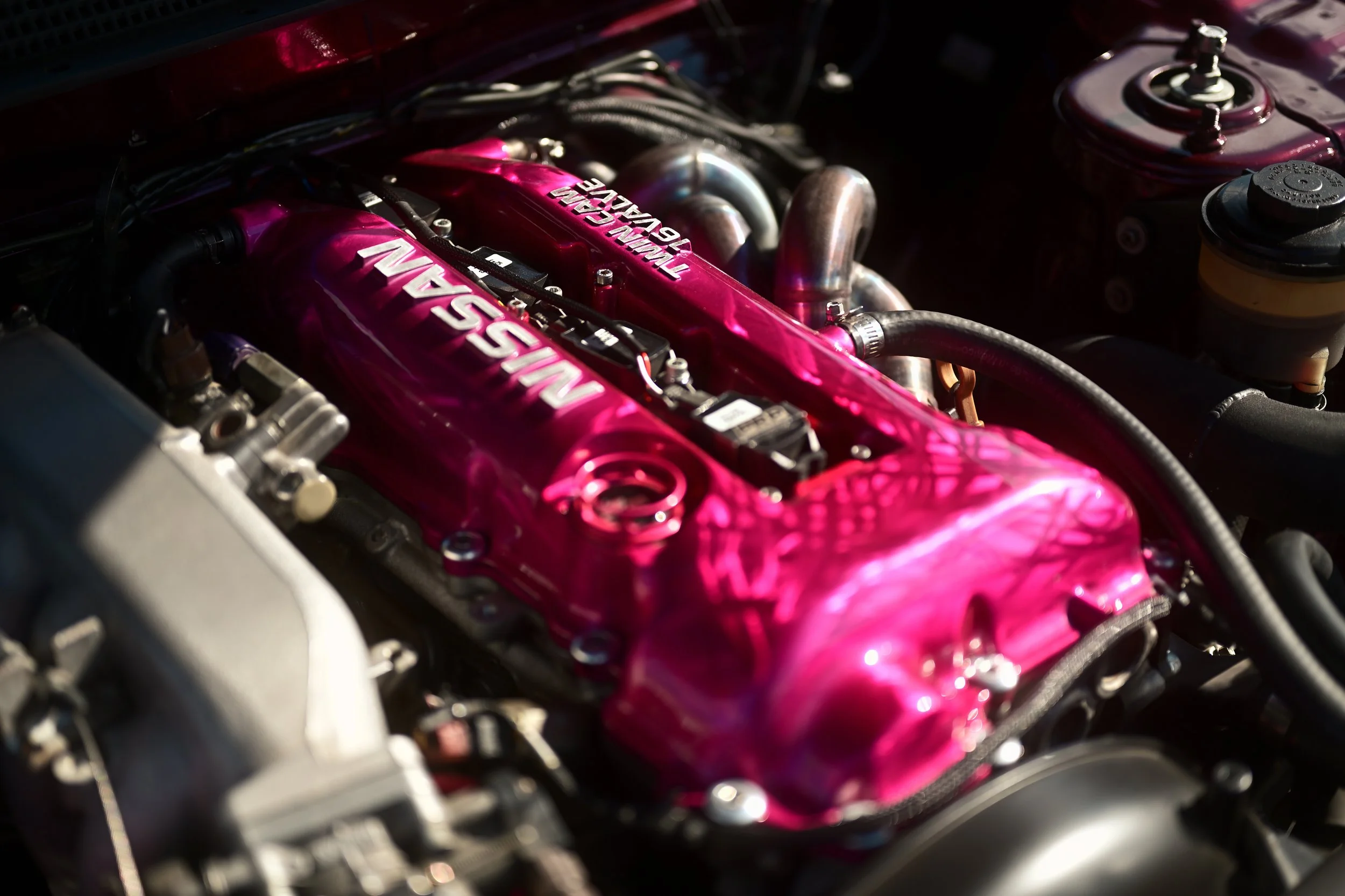 A close-up view of a car engine with a bright pink valve cover and piping, with the branding 'TWIN CAM 16 VALVE'.