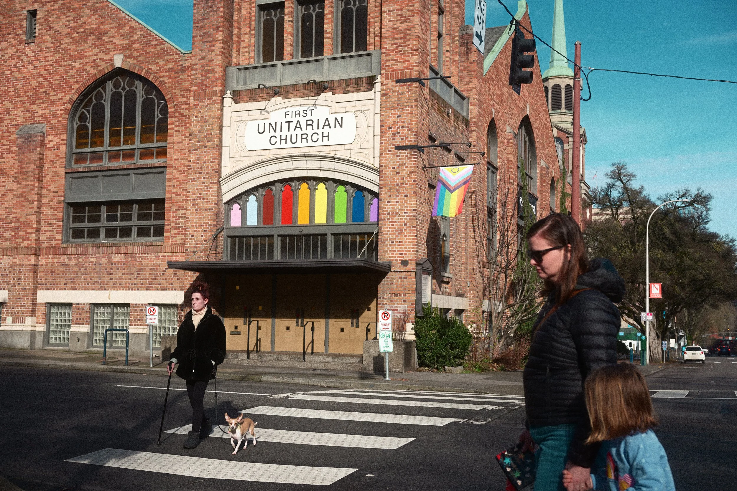 Historic brick First Unitarian Church with rainbow Pride flag at a city street intersection