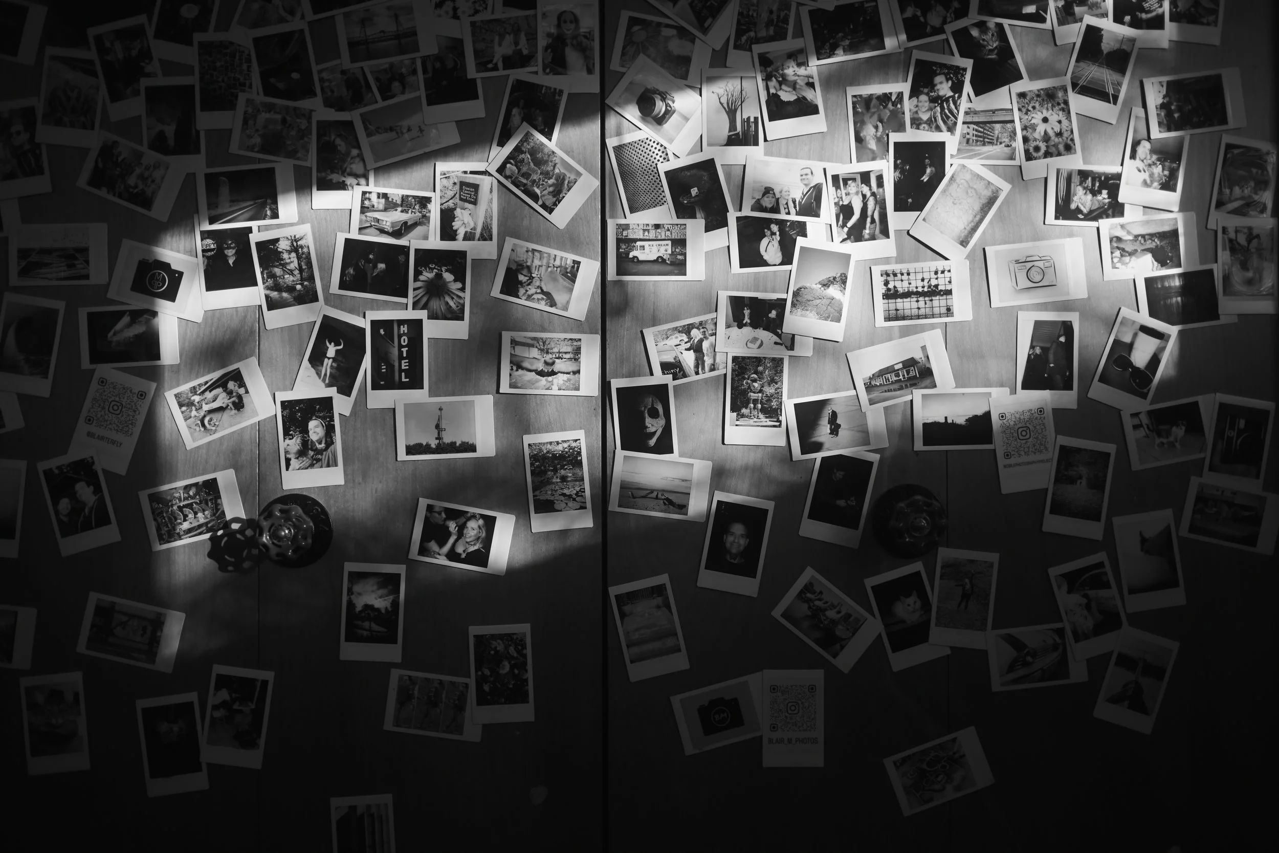 A collection of black and white photographs scattered on a wooden surface, including images of people, landscapes, objects, and QR codes.