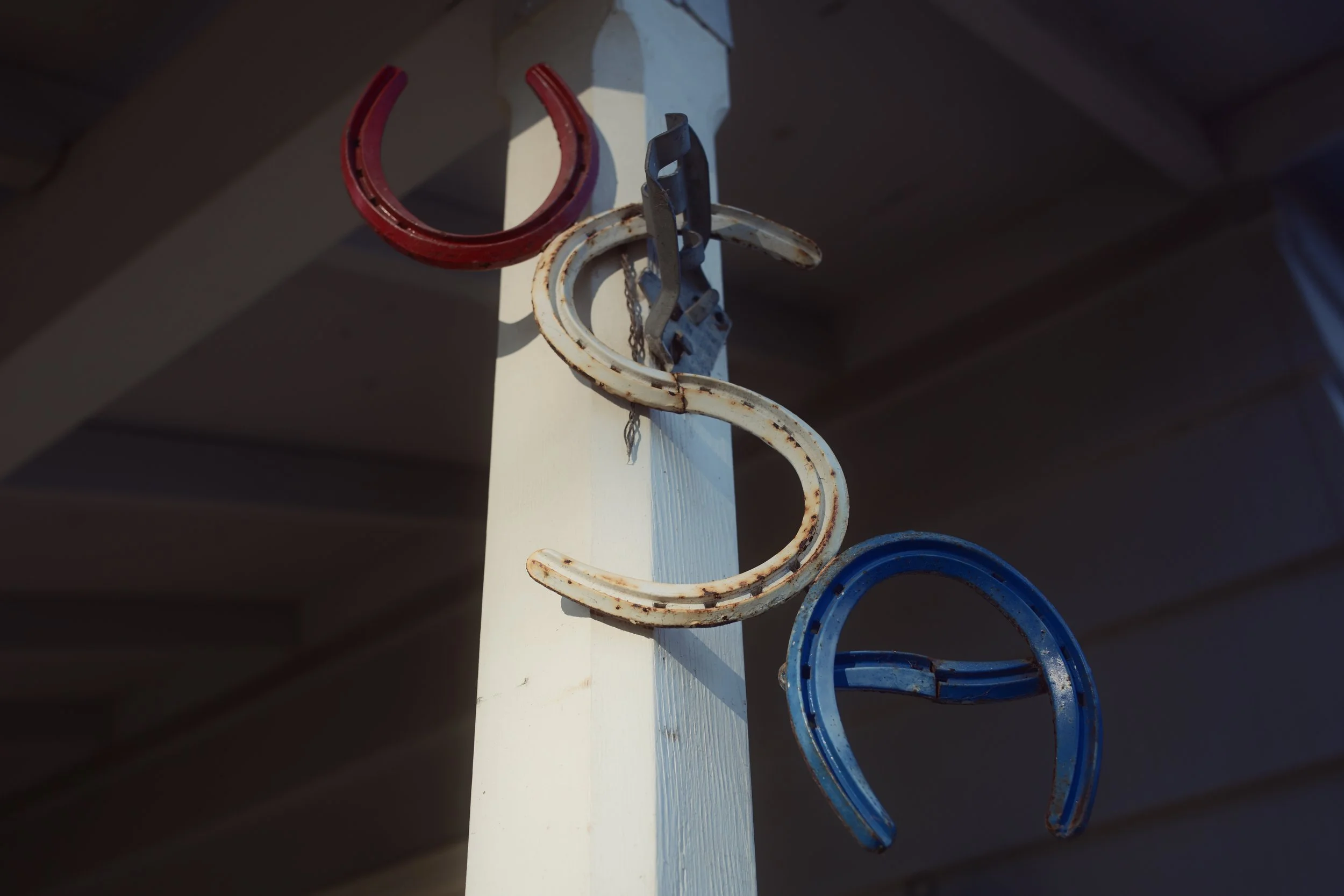 Colorful metal bangles hanging on a white vertical pole, with a dark background and partial roof in the scene.